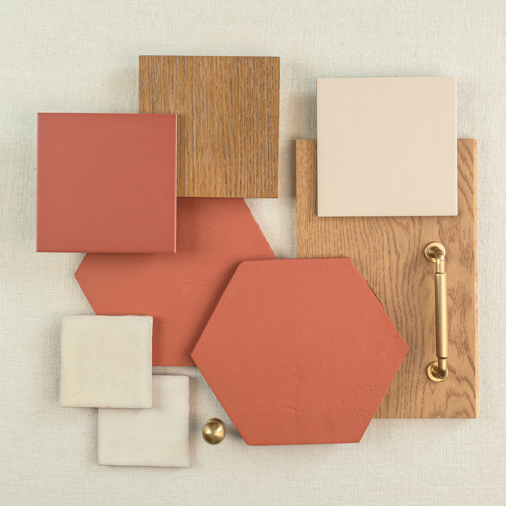 Flat lay of terracotta hexagon tiles, oak wood samples, cream ceramic squares, brass hardware, and beige fabric background