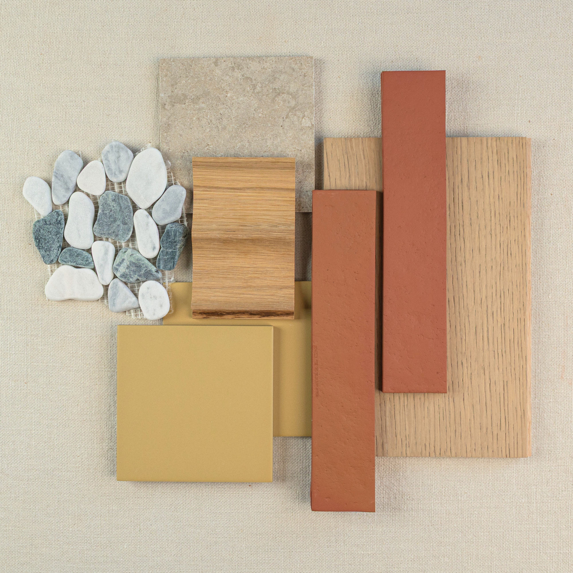 Flat lay of natural stone pebbles, beige stone tile, oak wood samples, terracotta tiles, and mustard square ceramic tile on fabric