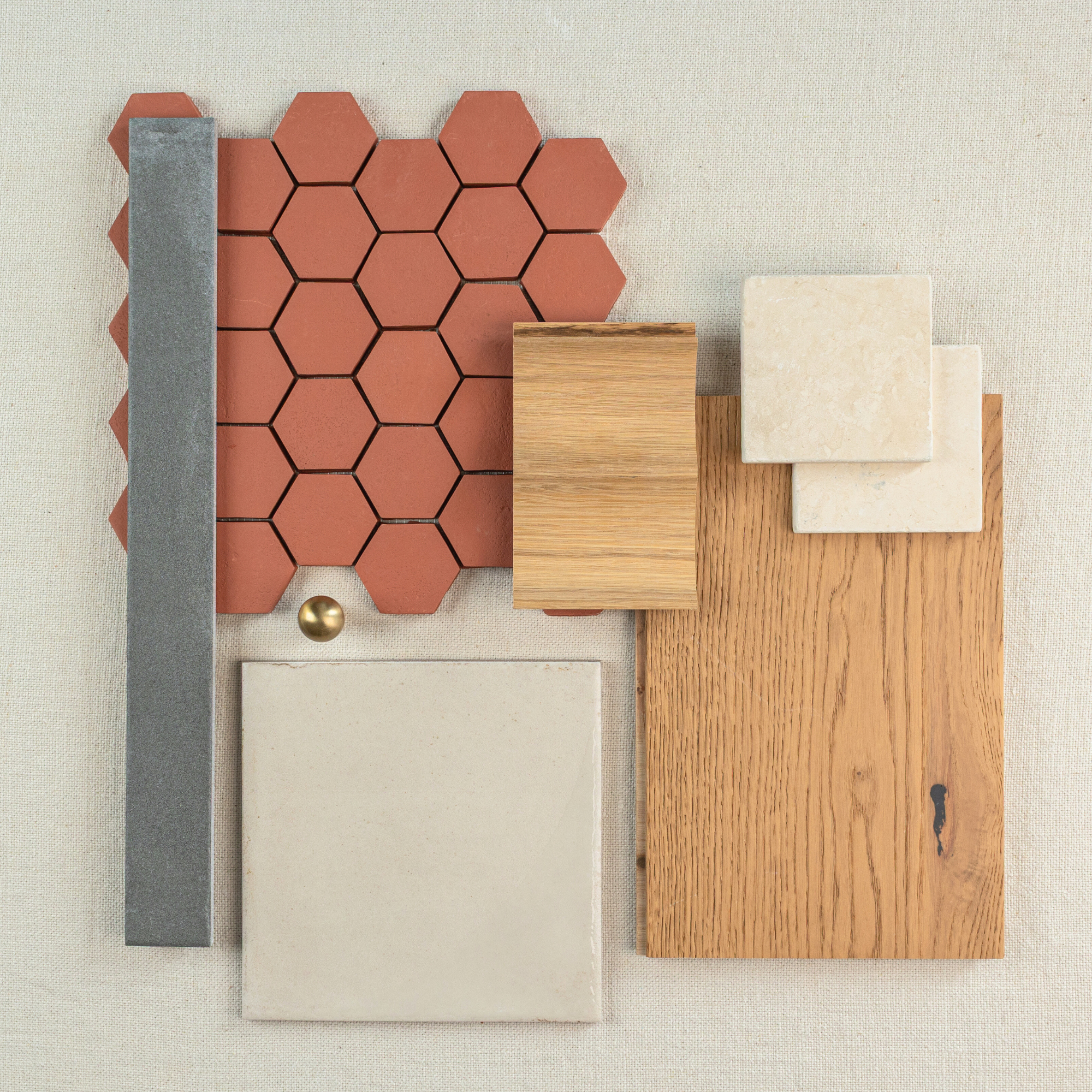 Flat lay of terracotta hexagonal tiles, oak wood plank, beige ceramic squares, gray tile strip, and brass hardware on fabric background