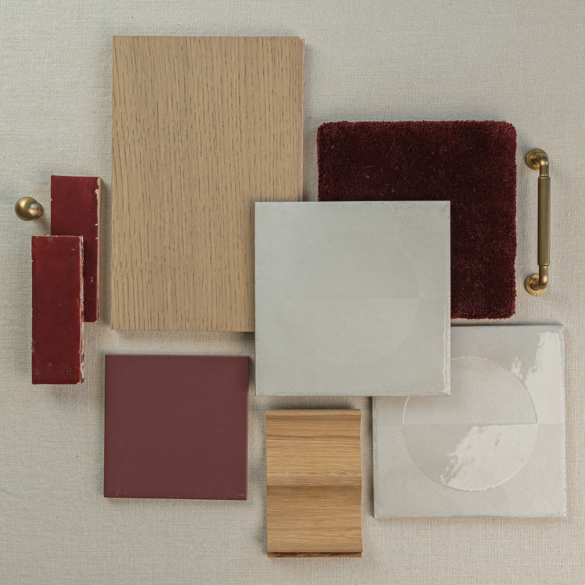 Flat lay of beige wood samples, matte and glossy ceramic tiles, deep red fabric and tile swatches with brass hardware on neutral background