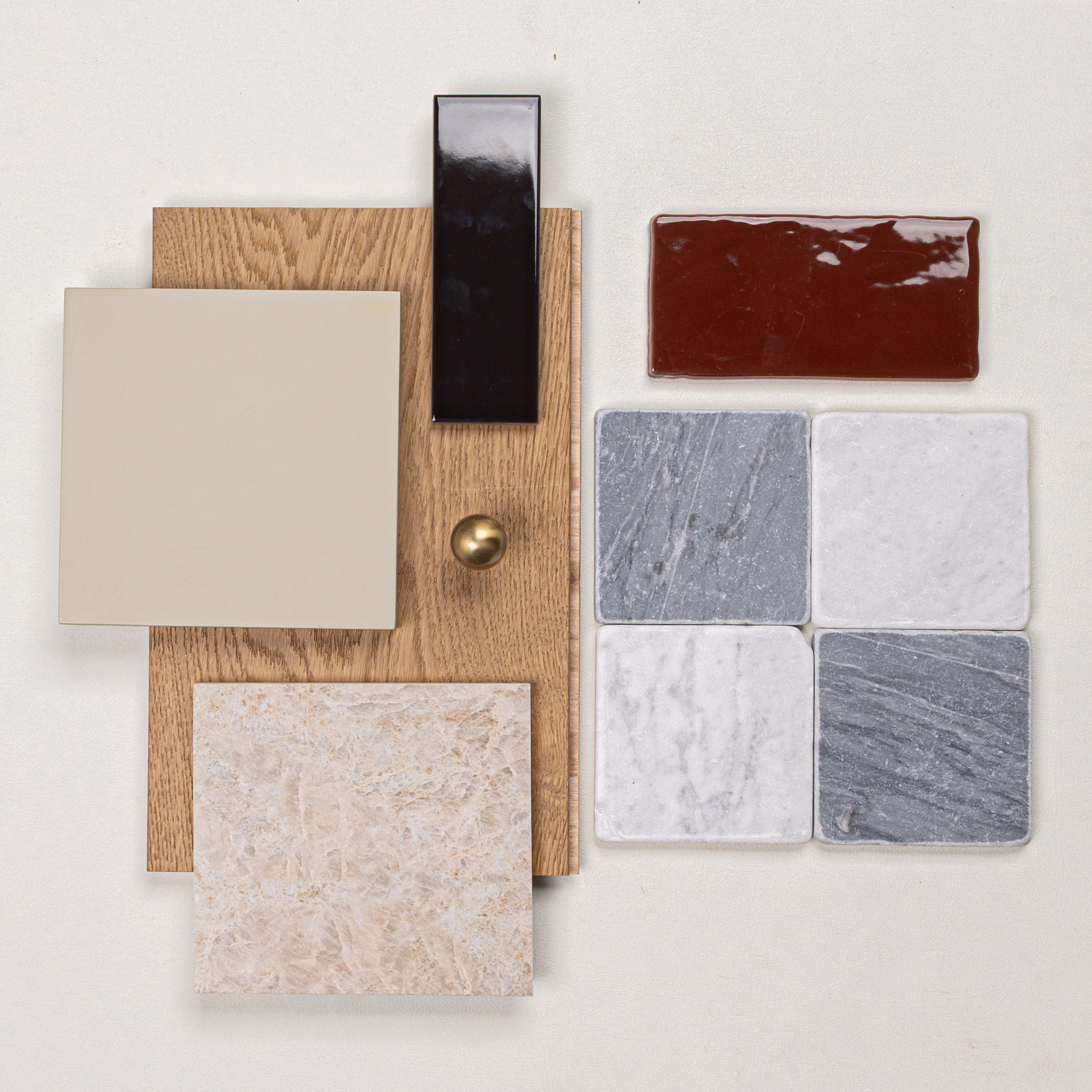 Arrangement of beige ceramic tiles, terracotta glazed tile, grey and white marble squares, oak wood sample, and brass knob on pale surface