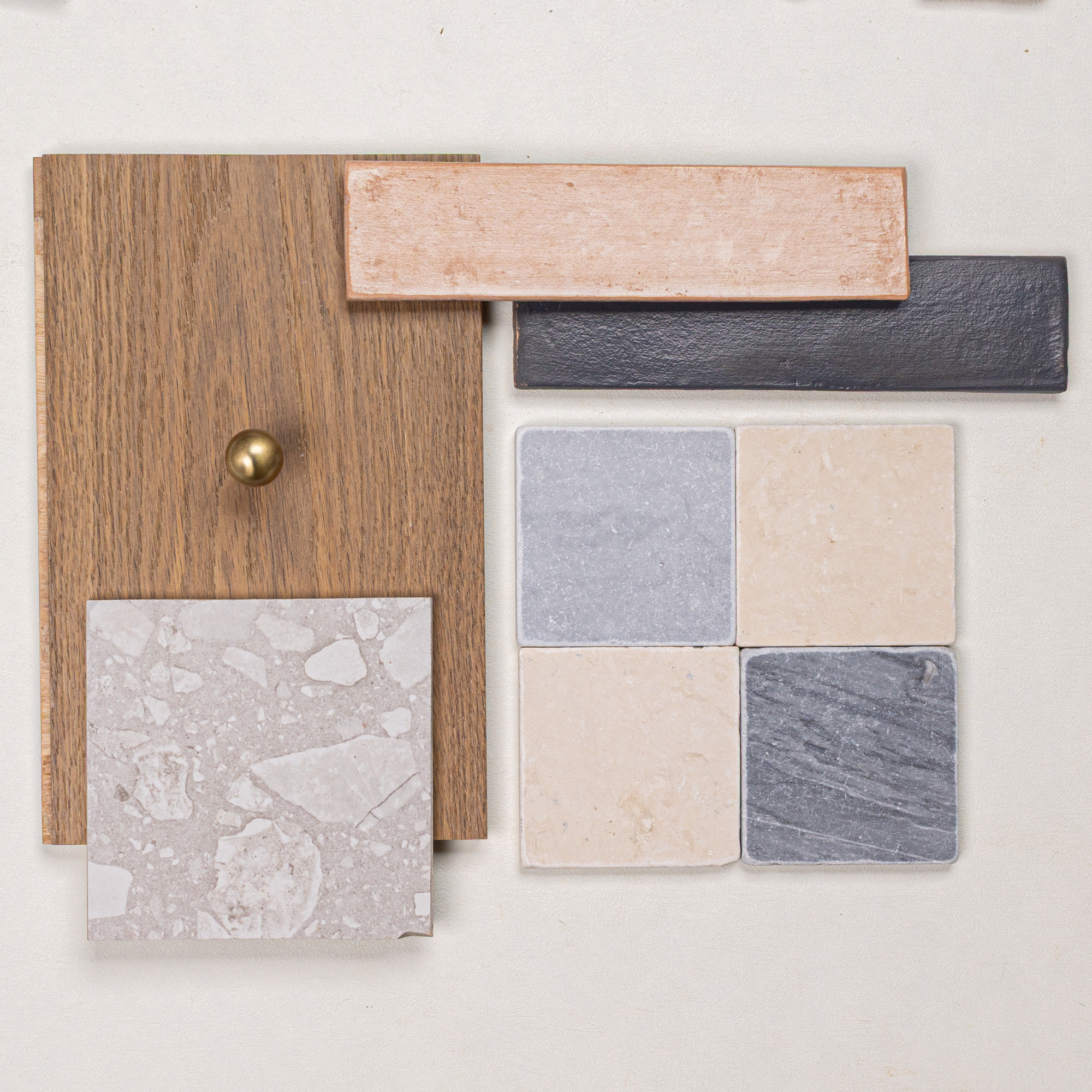 Collection of wood sample with brass knob, textured ceramic tiles in earthy tones, and natural stone tile swatches arranged on white surface