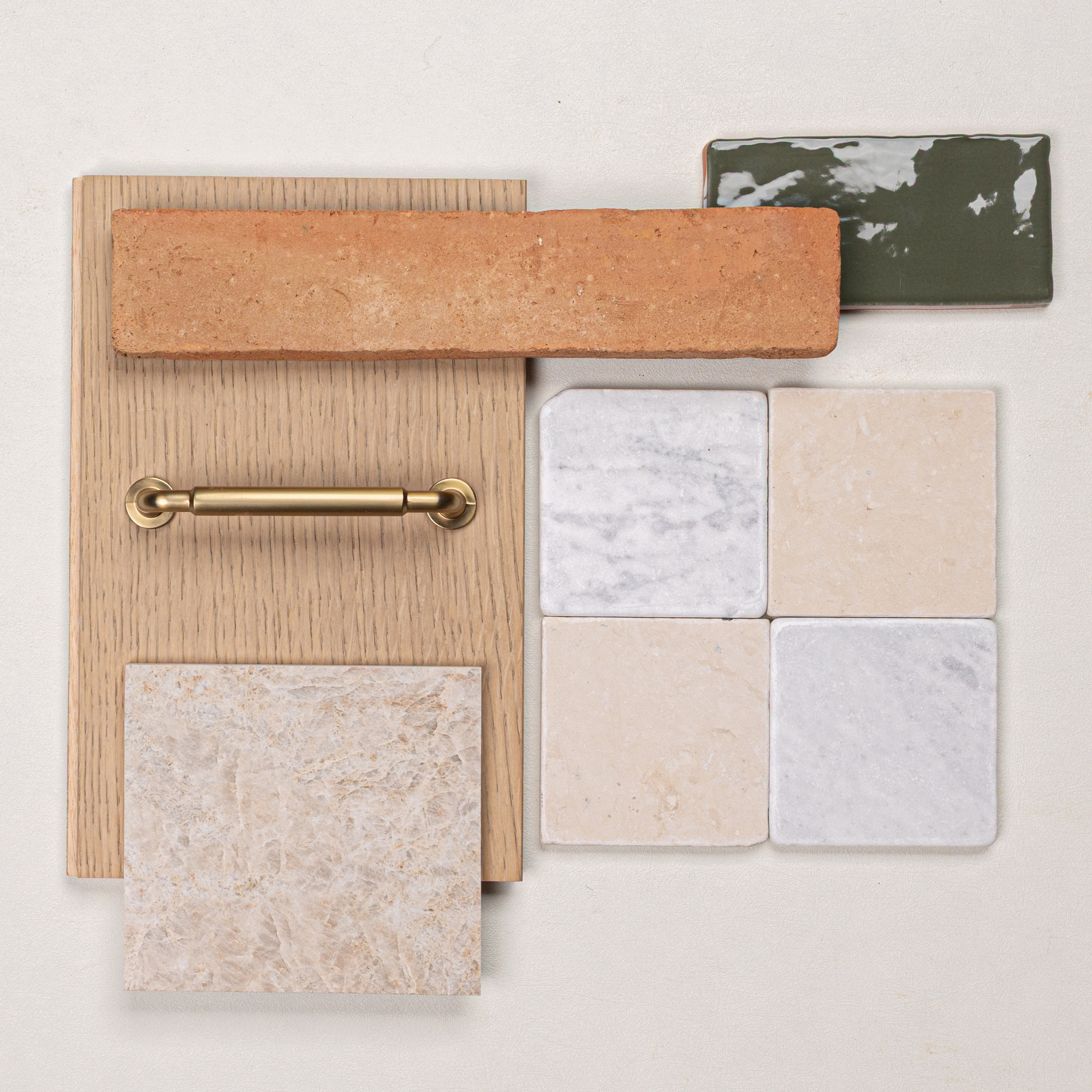 Flat lay of terracotta brick, green ceramic tile, beige and white marble tiles, oak wood sample, and brass hardware on light surface