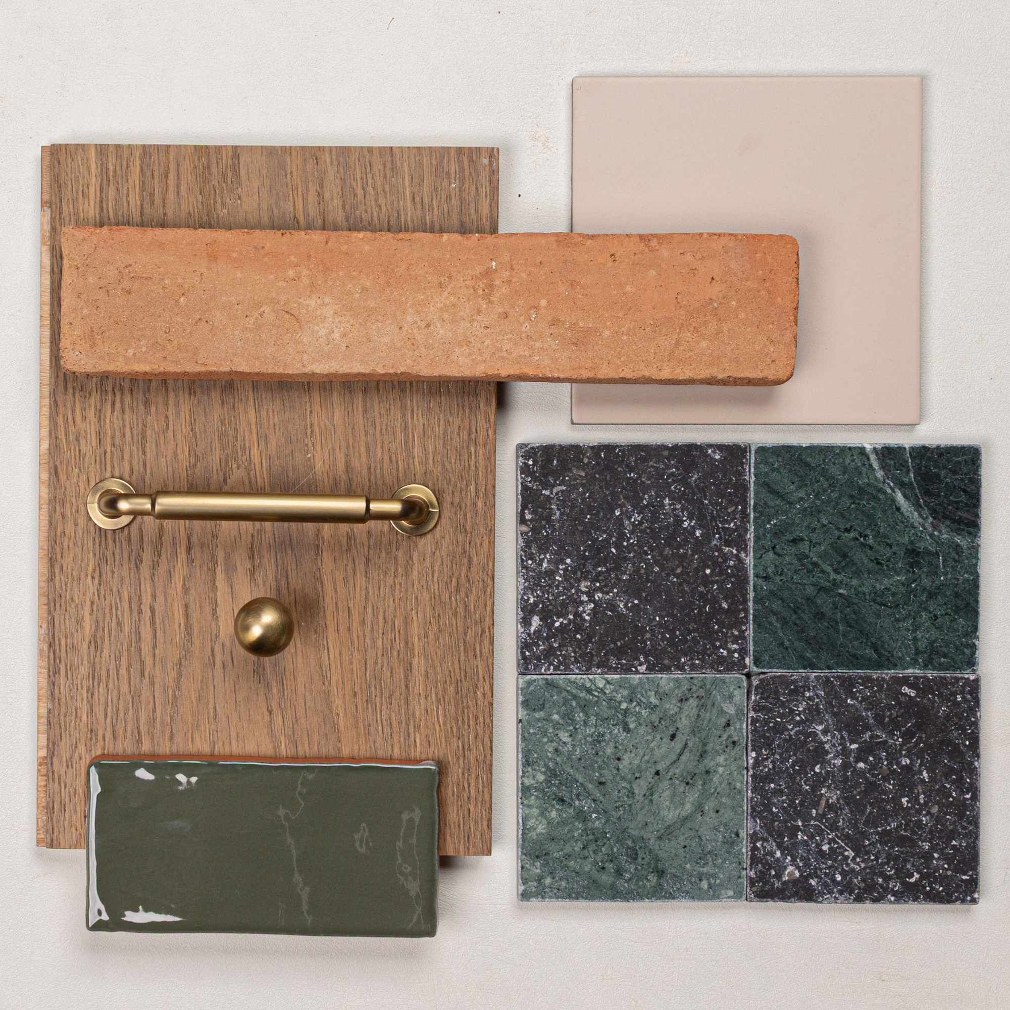Terracotta tile with porcelain tile, oak wood sample, green and black marble tiles, and brass hardware pieces arranged on white surface