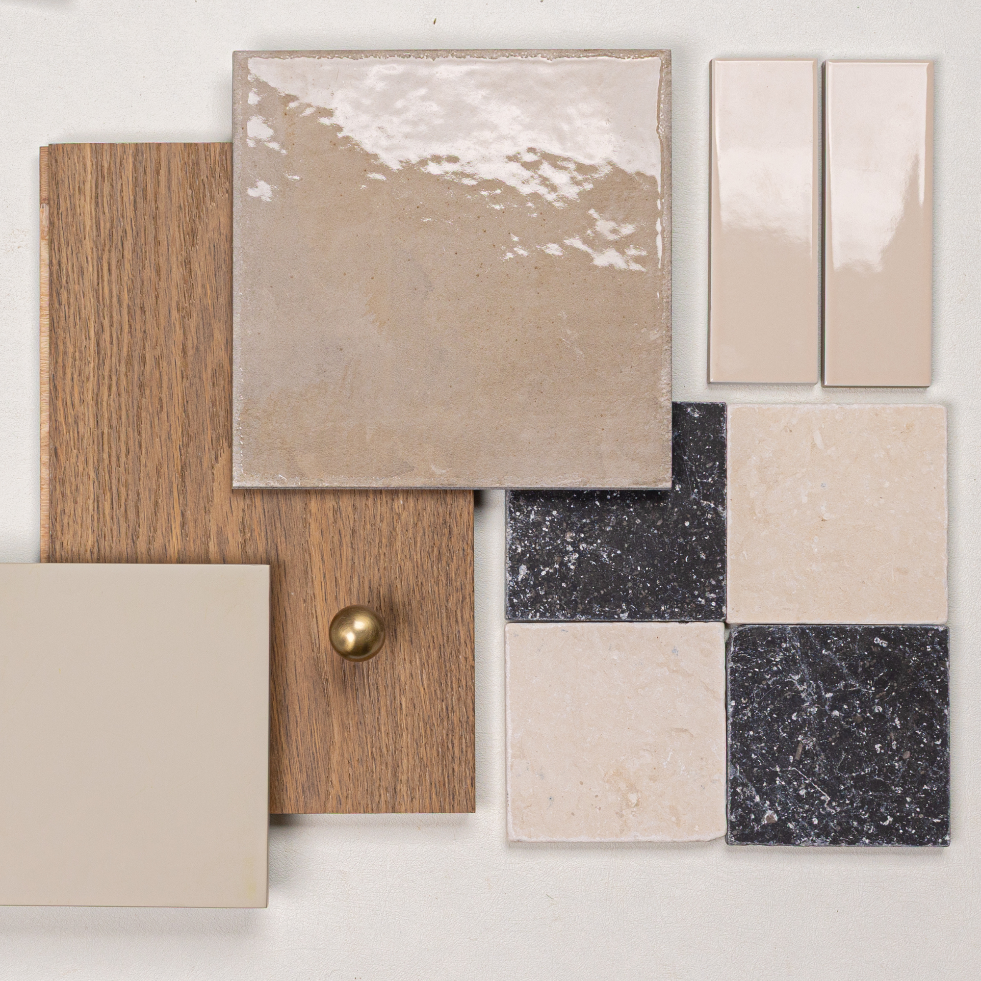 Glossy ceramic and porcelain tile samples paired with oak wood and a brass knob on a light neutral background