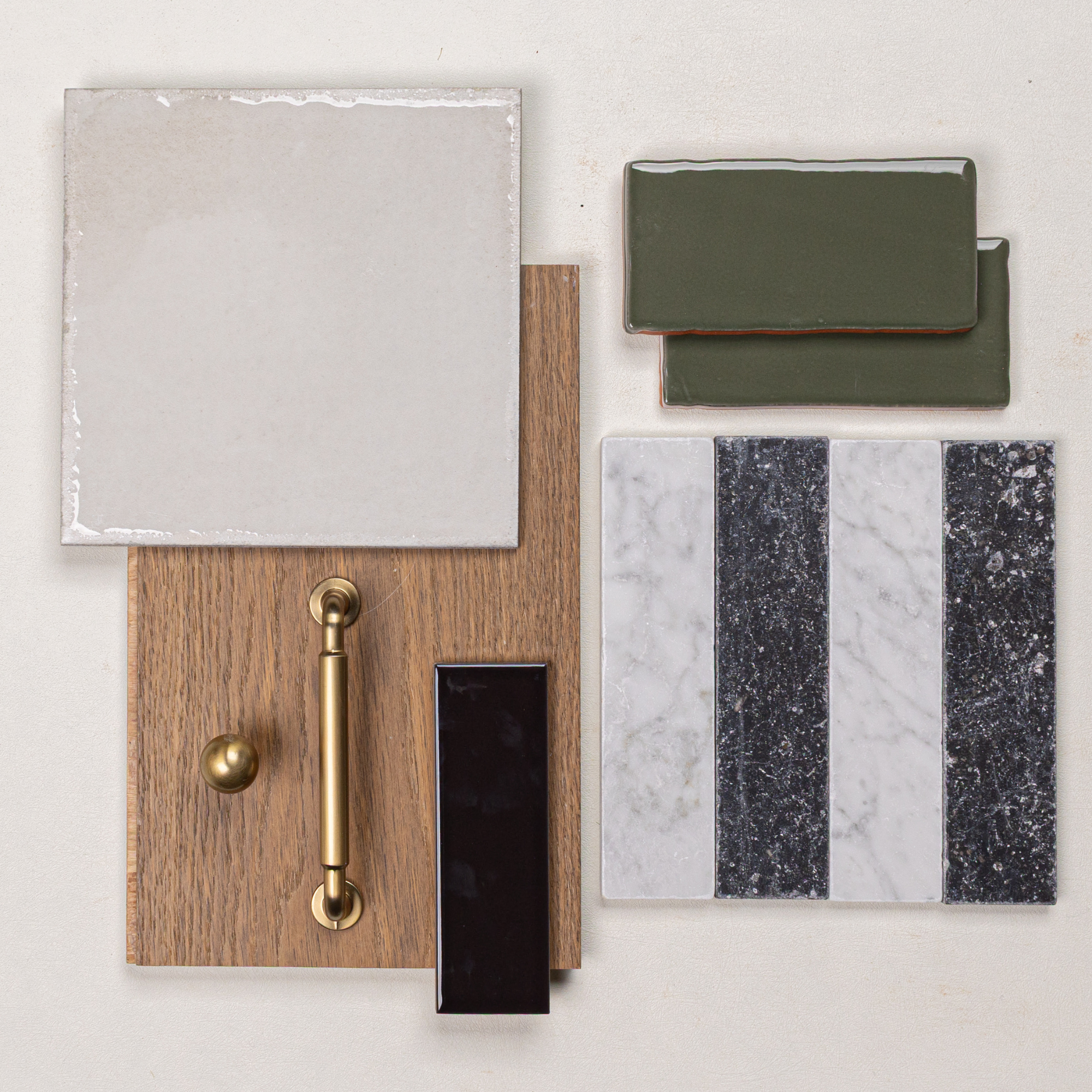 Flat lay of ceramic tiles, green glazed tiles, oak wood sample, brass hardware, and striped marble tile on a light background