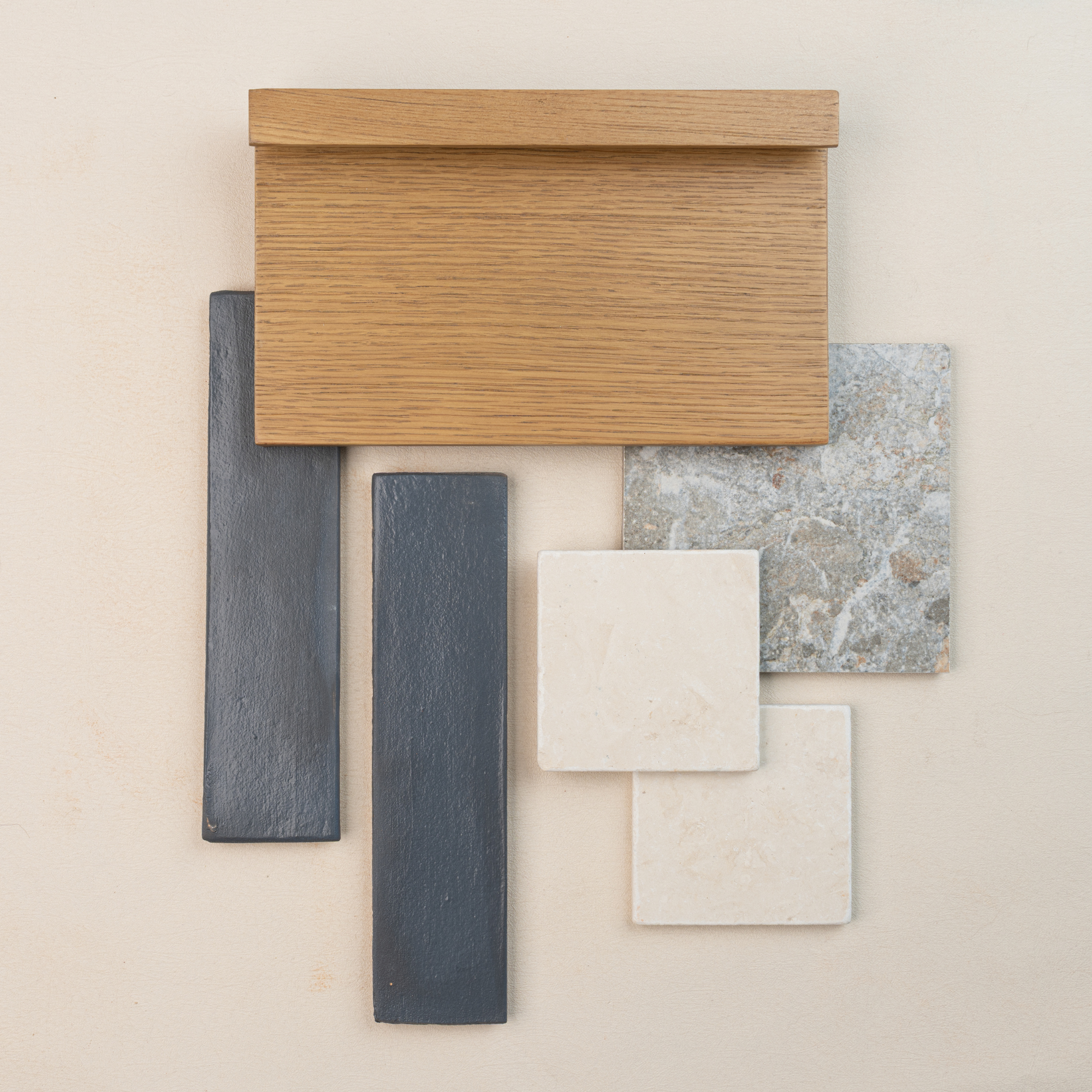 Flat lay of oak wood sample with textured gray rectangular tiles and square natural stone tiles on light background