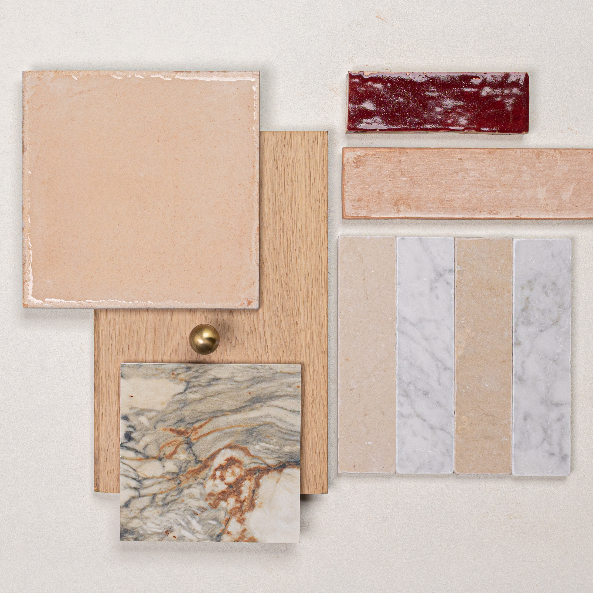 Flat lay of soft beige ceramic tile, oak wood sample with brass knob, marbled stone, textured red and beige elongated tiles, and marble mosaic strips