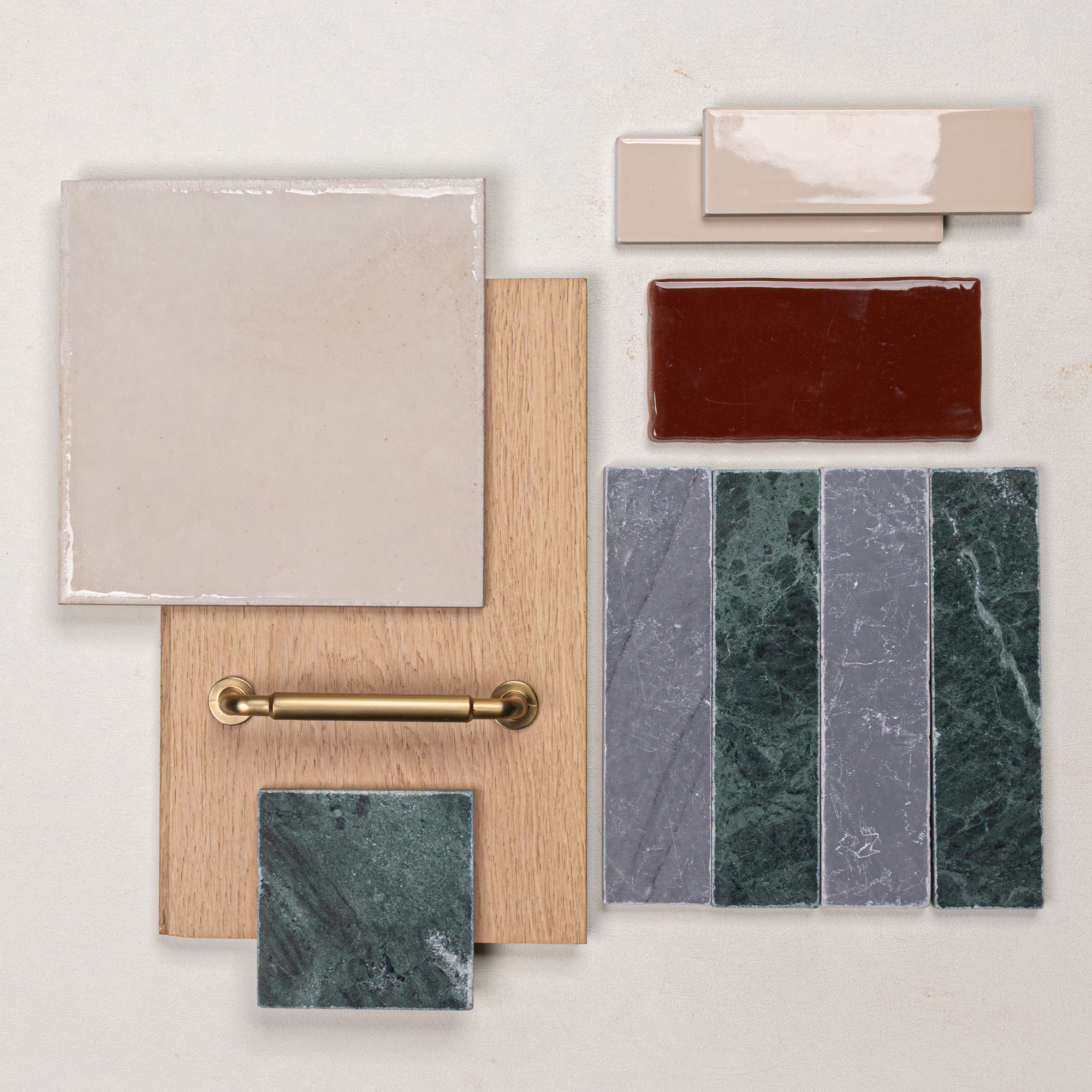 Arrangement of beige ceramic tile, green marble samples, red and cream glazed tiles, light oak wood, and brass hardware on neutral background