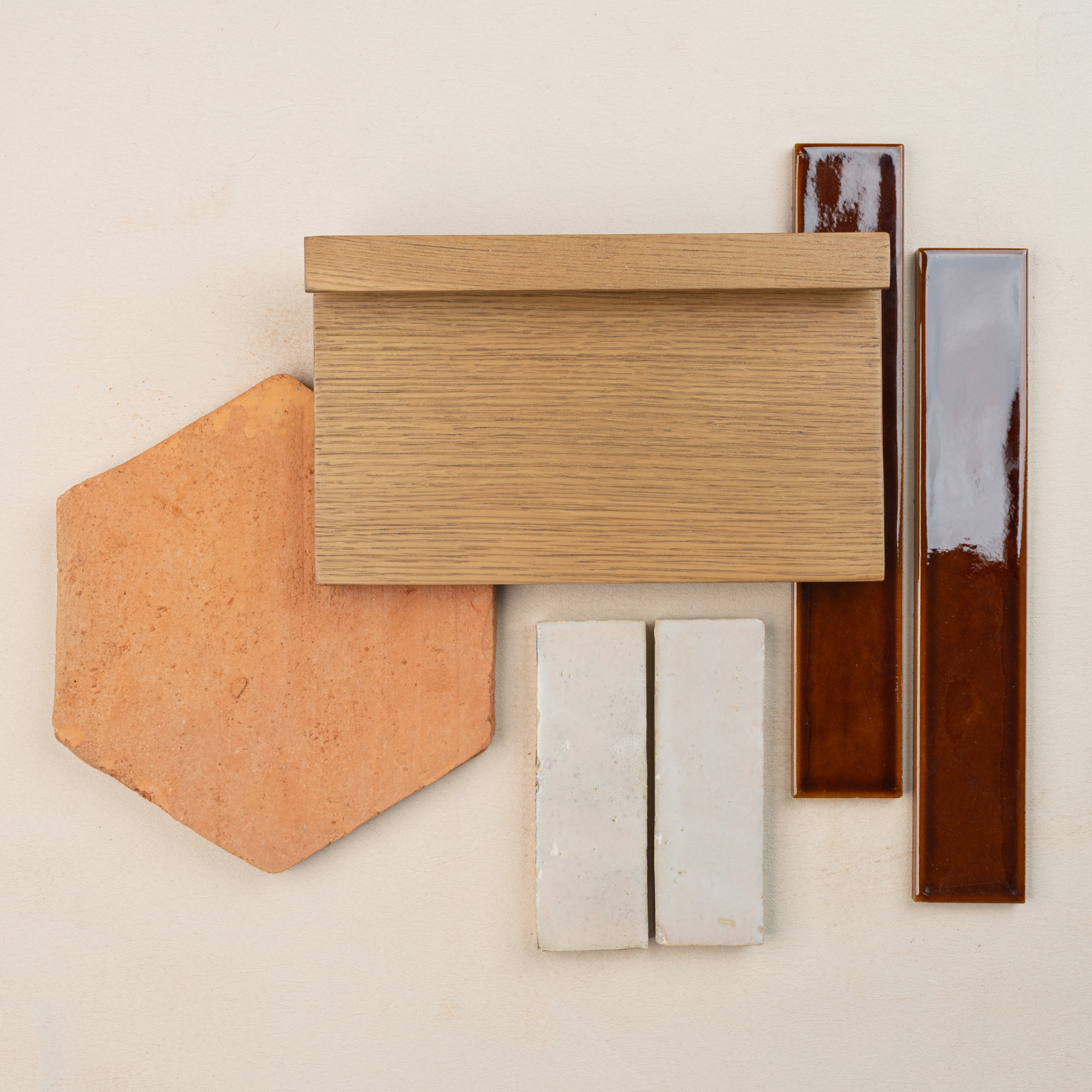 Flat lay of terracotta hexagonal tile, oak wood sample, two white bricks, and glossy brown ceramic tiles on pale background