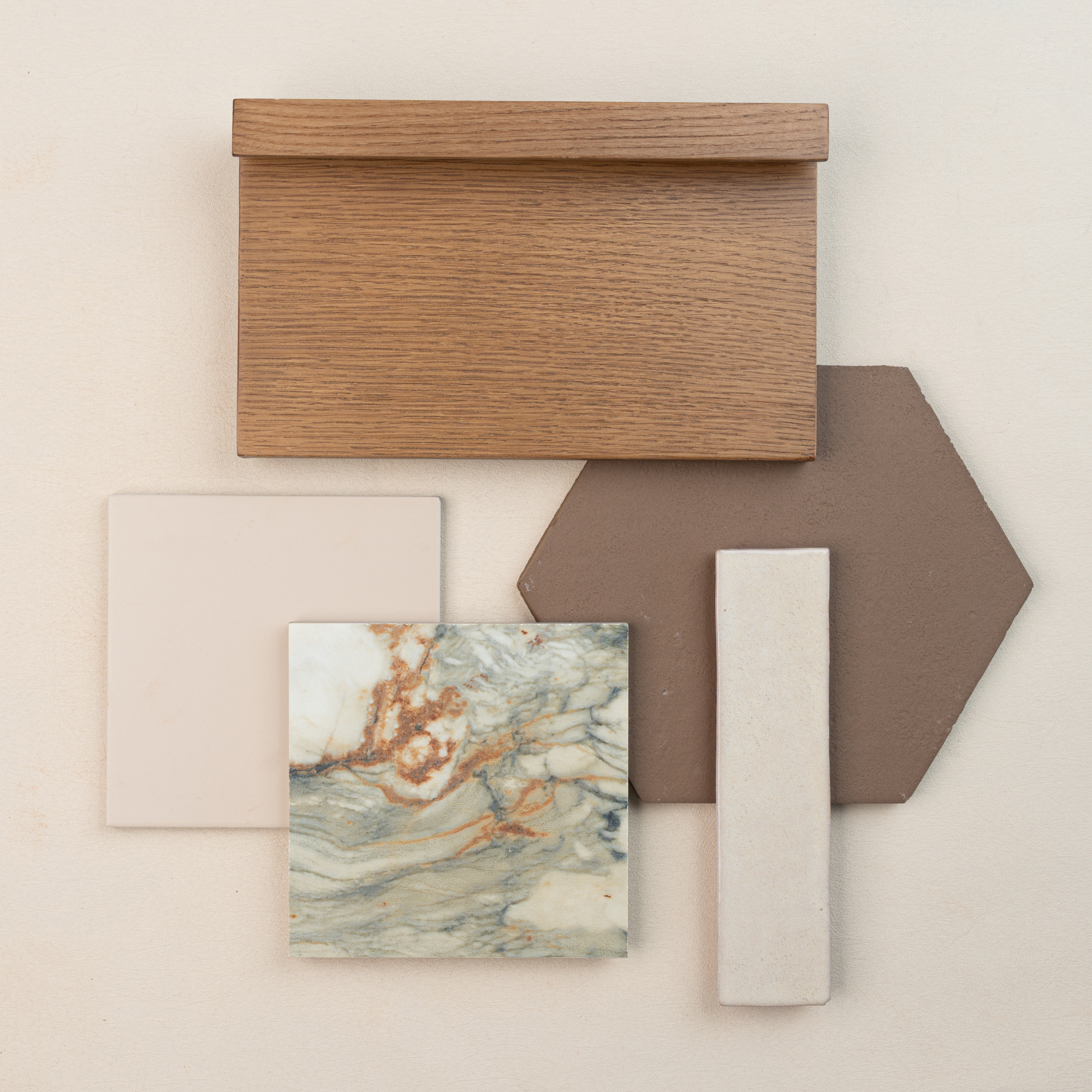 Flat lay of oak wood sample with brown hexagonal tile, marble-look ceramic, cream rectangular tile, and pale square porcelain tile