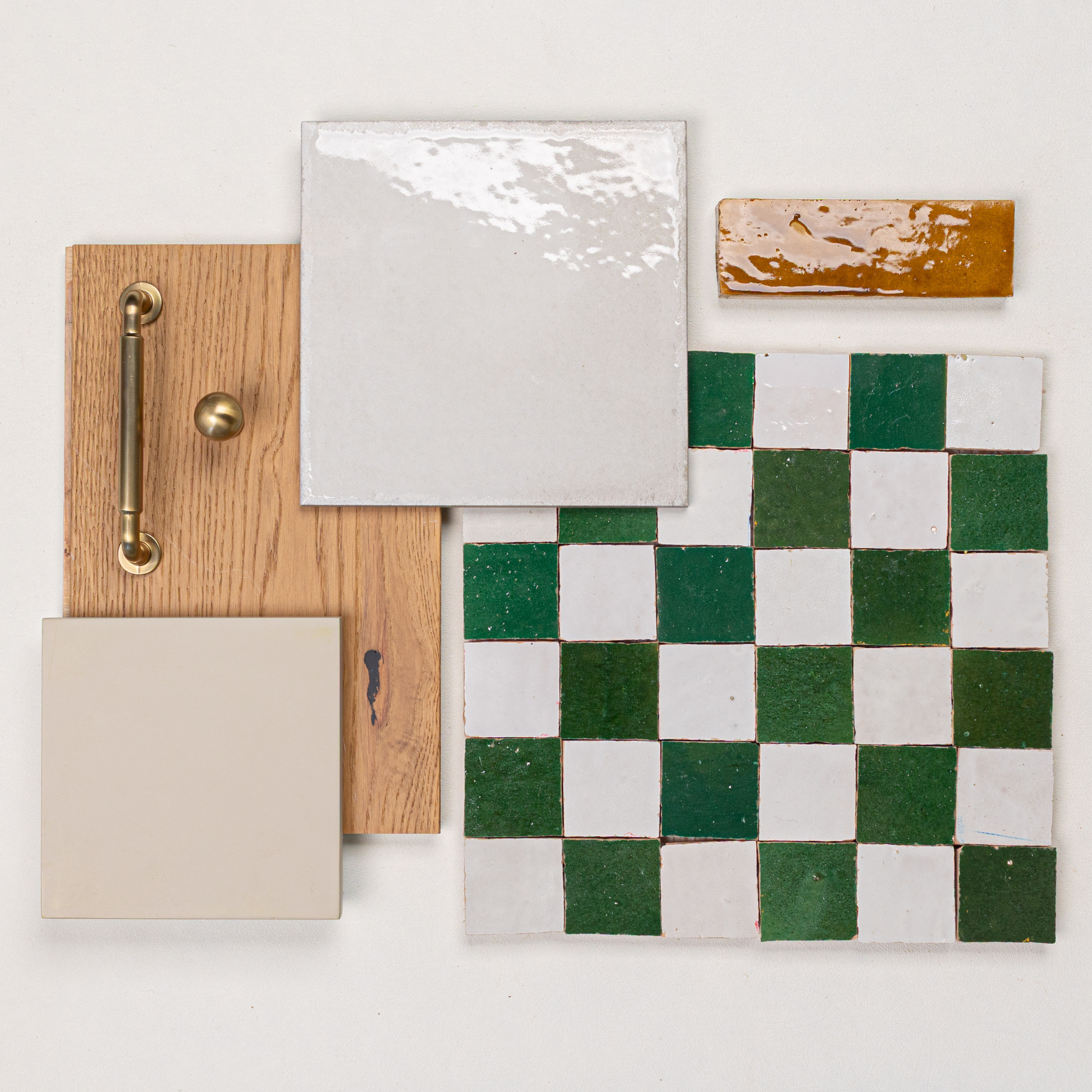 Flat lay of checkerboard green and white tiles, beige tile, oak wood with brass handle and knob, and a small amber tile