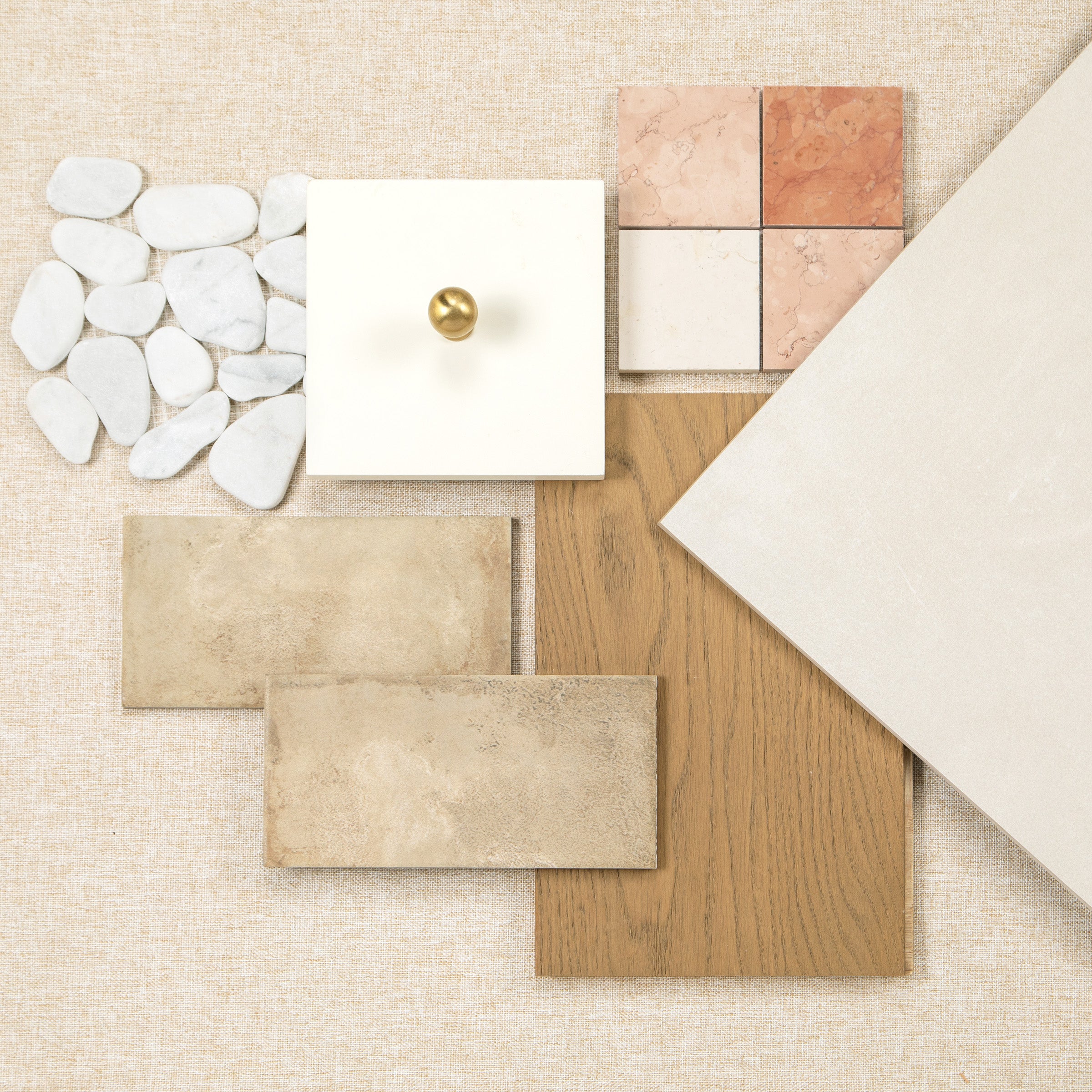 Flat lay of tile samples, oak flooring, white pebbles, and a brass cabinet knob
