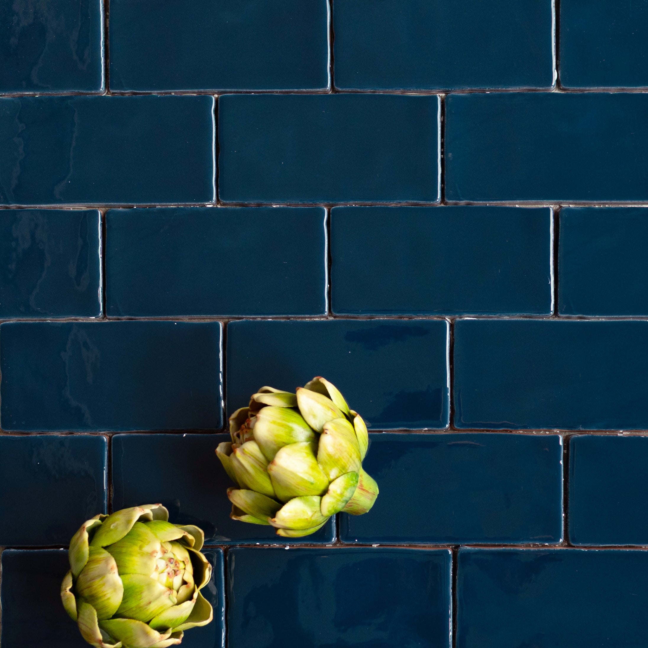 Glossy deep navy ceramic tiles with irregular edges arranged in a brick pattern with two fresh artichokes on top