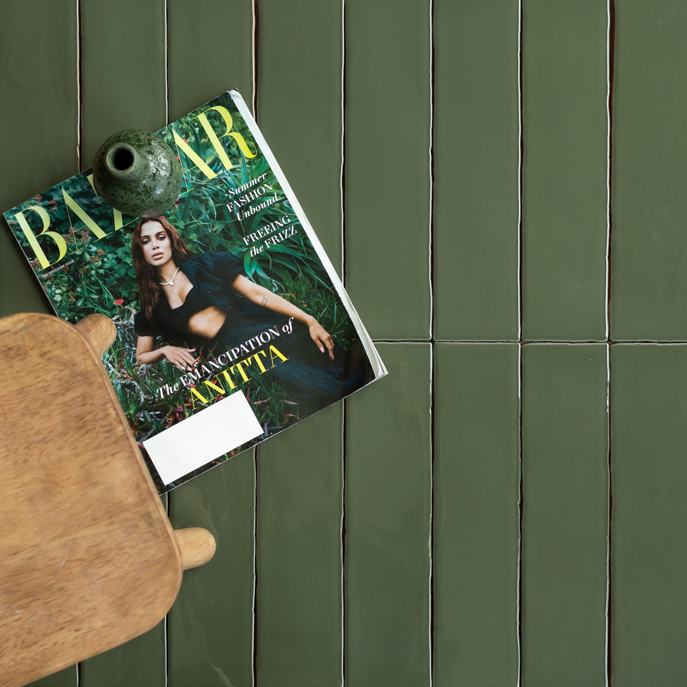 Glossy olive green ceramic tiles with slight color variation arranged in an irregular grid pattern next to wood and ceramic decor