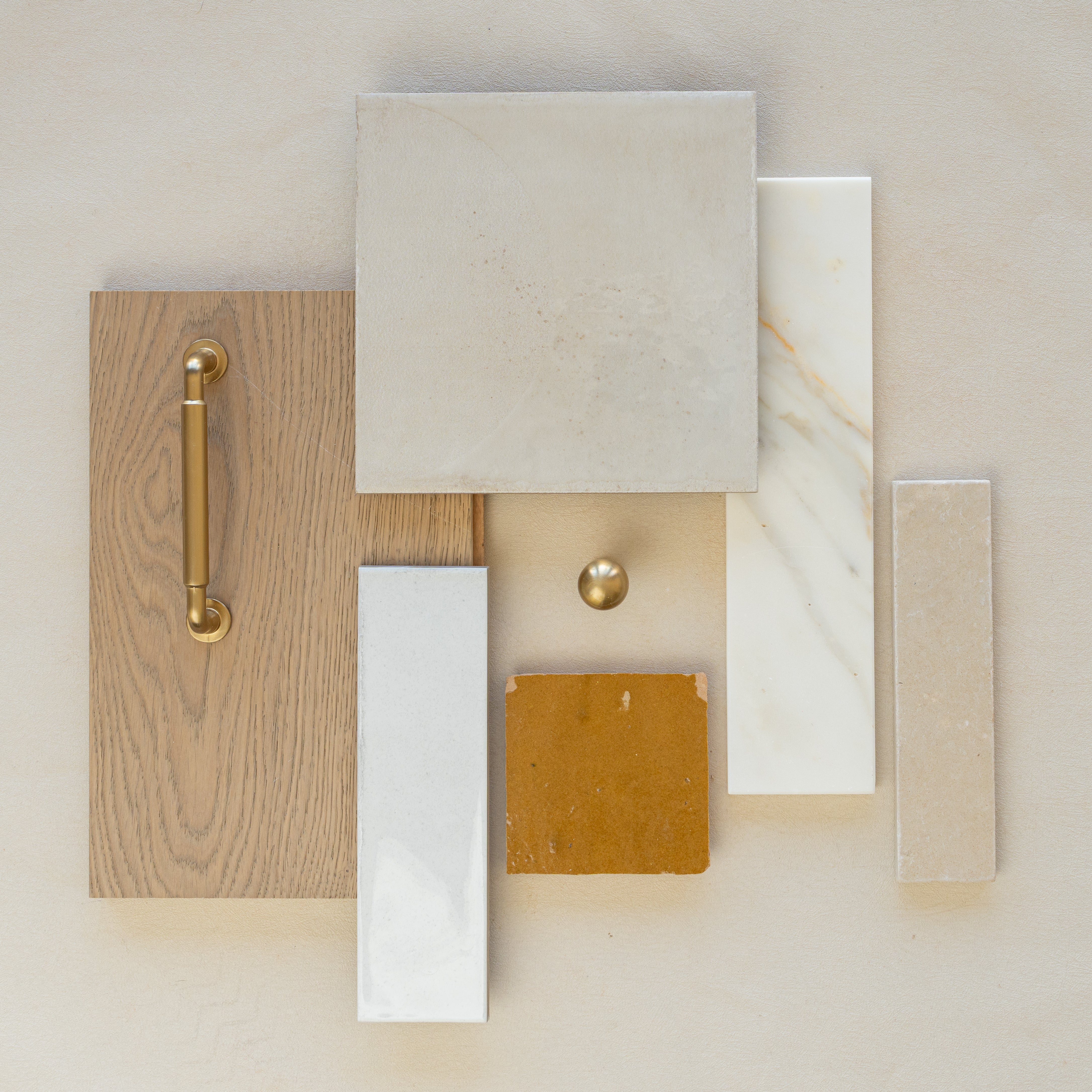 Flat lay of oak wood with brass handle, beige square and rectangular ceramic and porcelain tiles, and mustard tile on cream surface