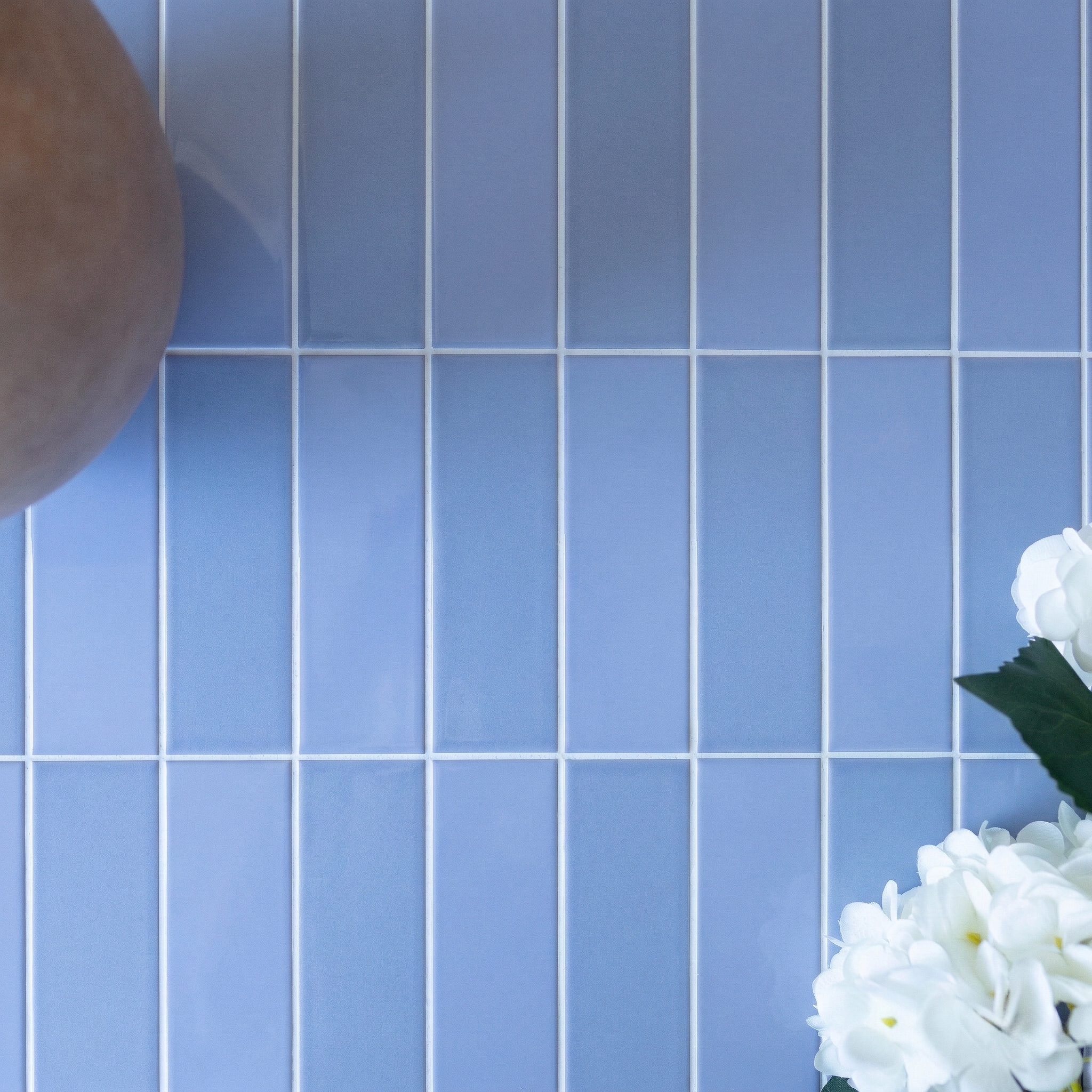 Blue rectangular ceramic tiles with white grout beside a brown vase and white flowers on the right side