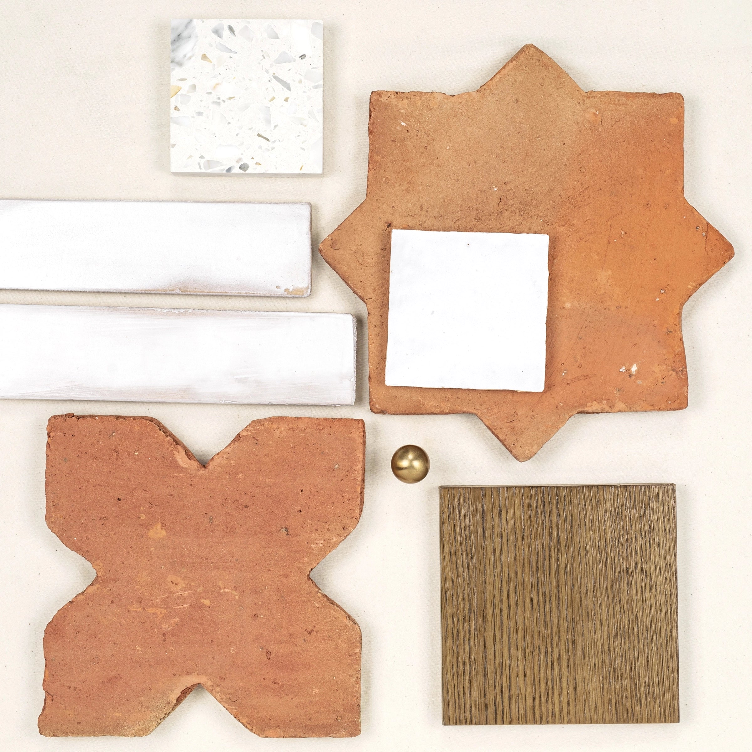 Assortment of terracotta and white ceramic tiles with a wood sample and brass knob on a pale surface