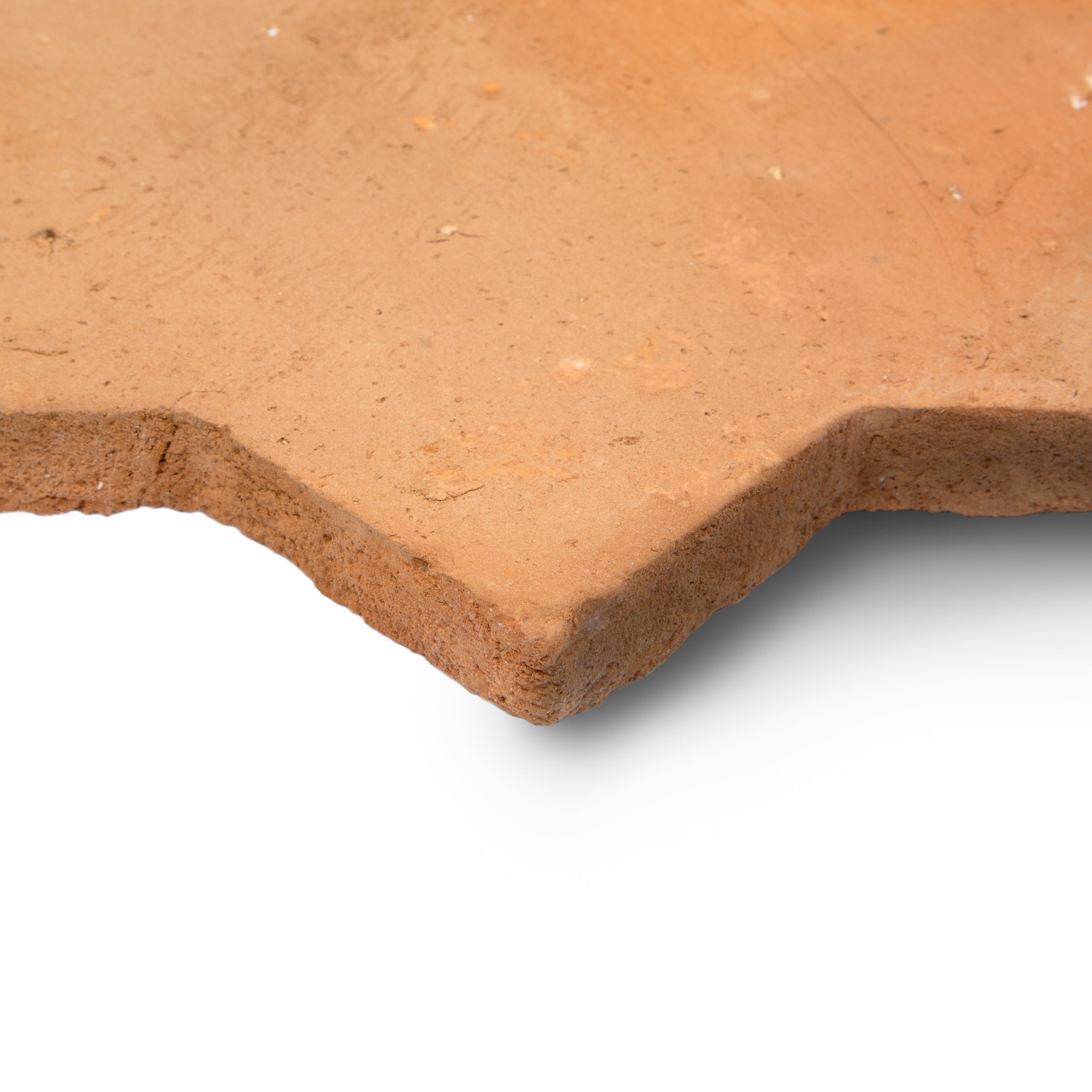 Close-up of textured terracotta tile corner with warm natural hues and handcrafted rustic edge on white background