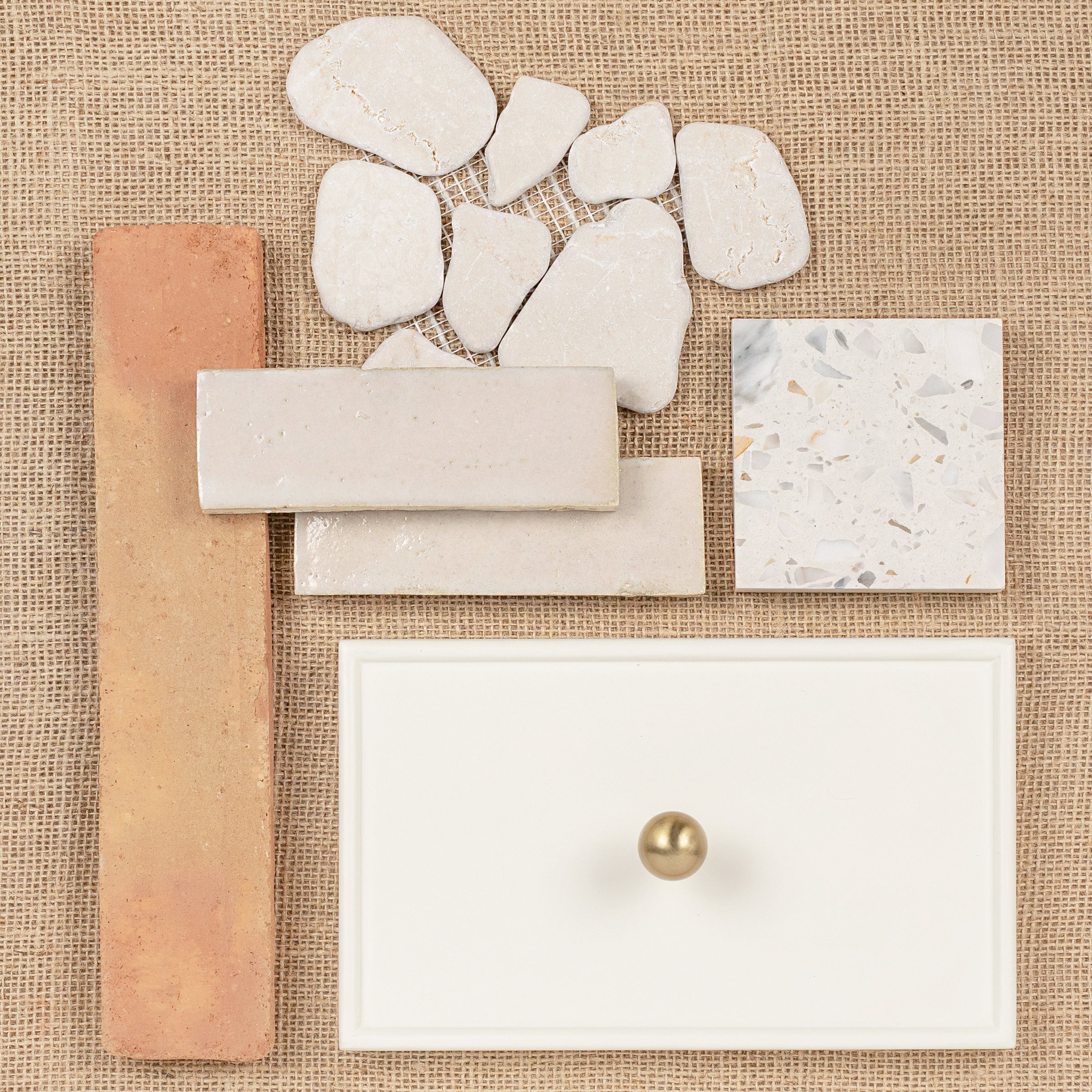 Flat lay of various ceramic and porcelain tiles with a white drawer front featuring a brass knob on burlap background
