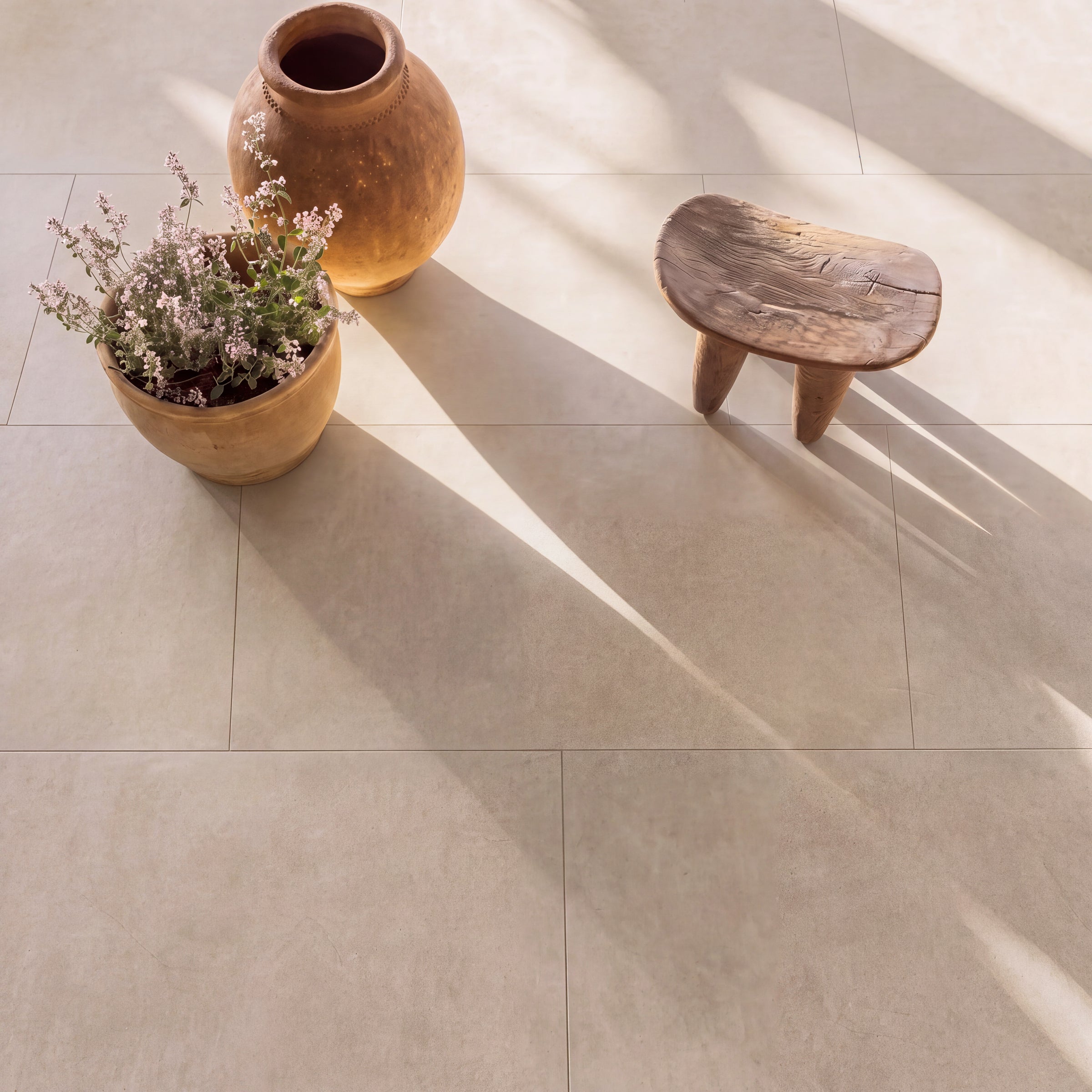 Large beige floor tiles with a potted plant ceramic vase wooden stool and sunlight shadows