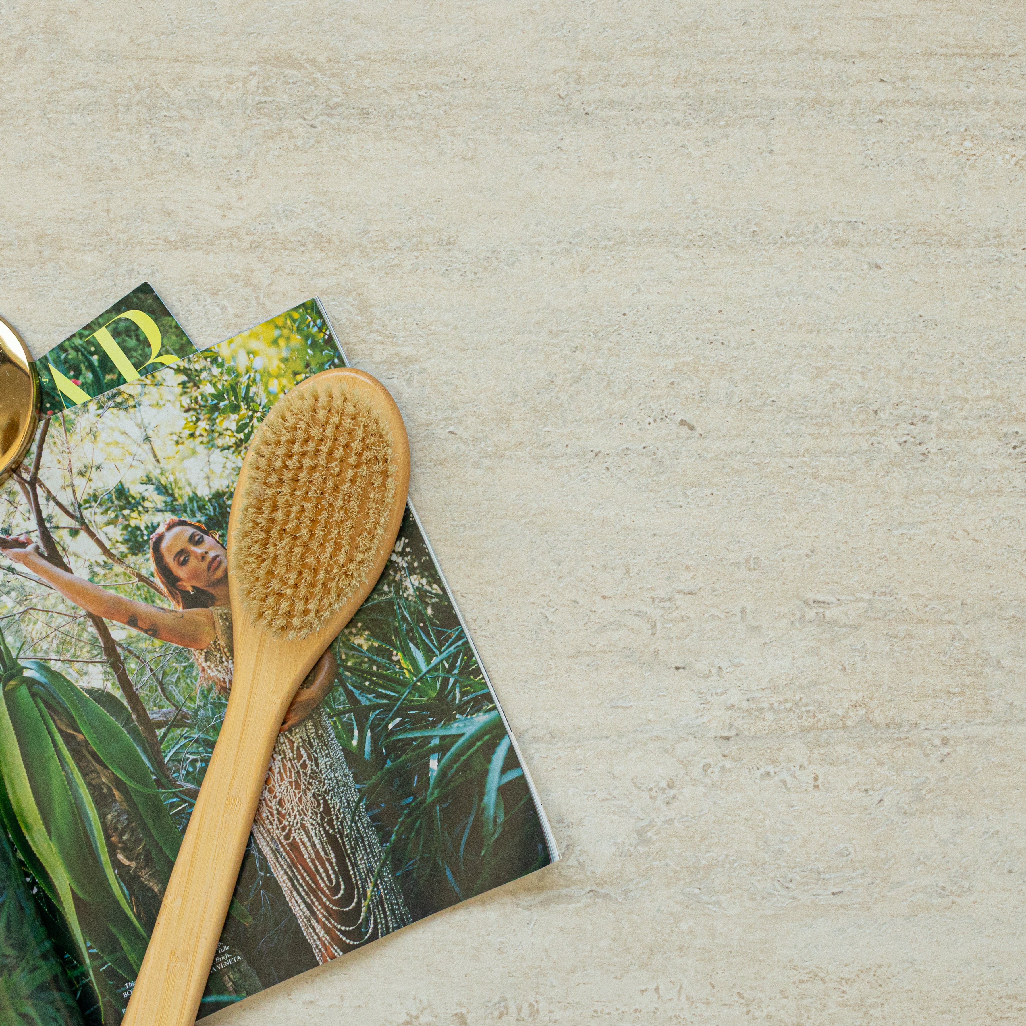 Beige travertine-look porcelain tile background with a wooden body brush and nature-themed magazine partially visible on the side