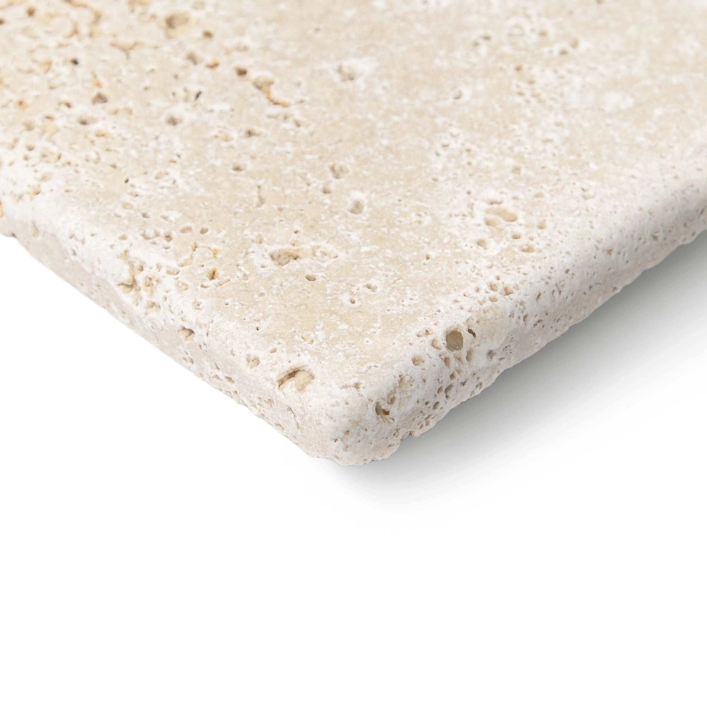 Close-up of a light beige travertine tile with a tumbled surface showing natural pitting and irregular edges