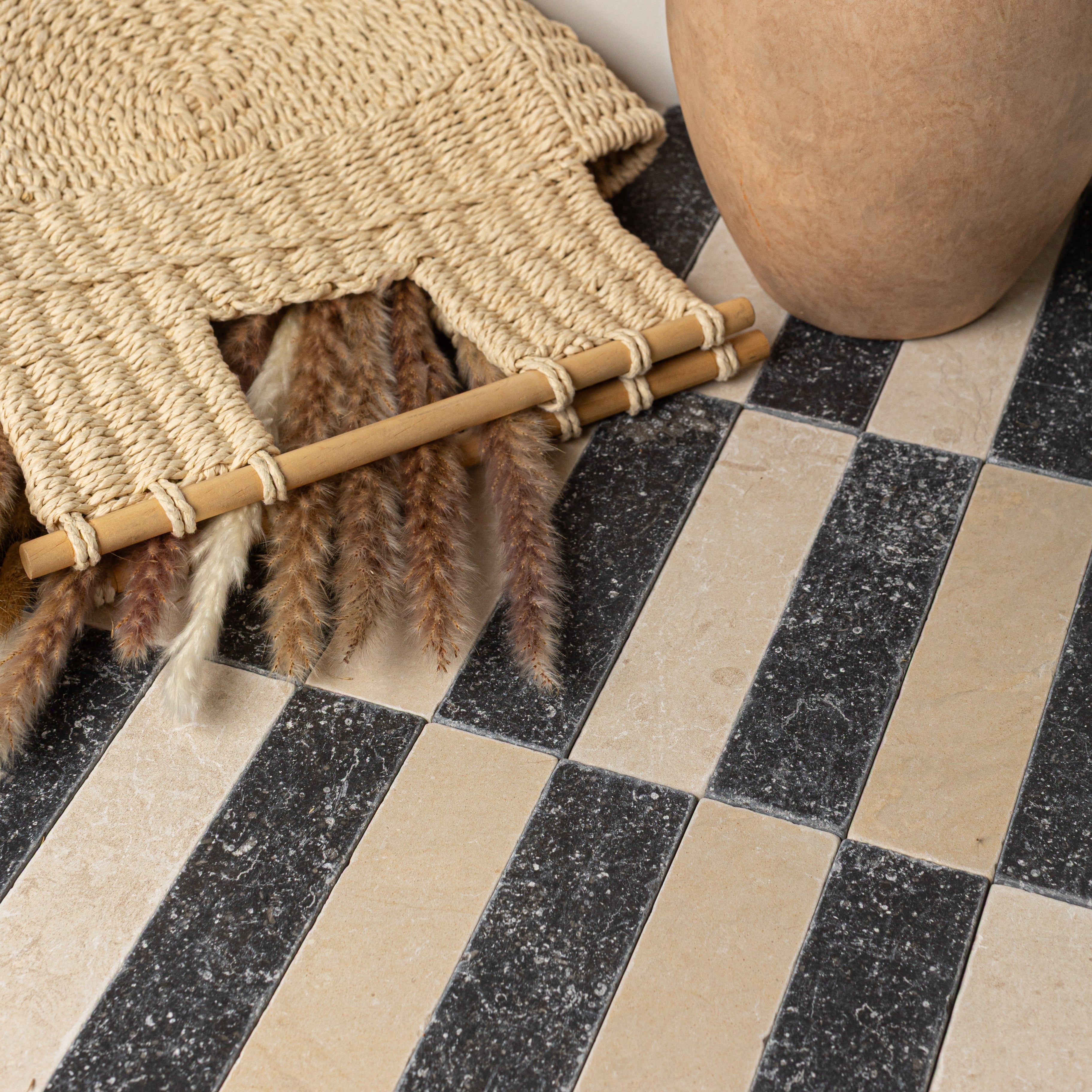 Rectangular ceramic tiles in alternating black and beige hues with a textured surface alongside natural woven decor and dried grasses