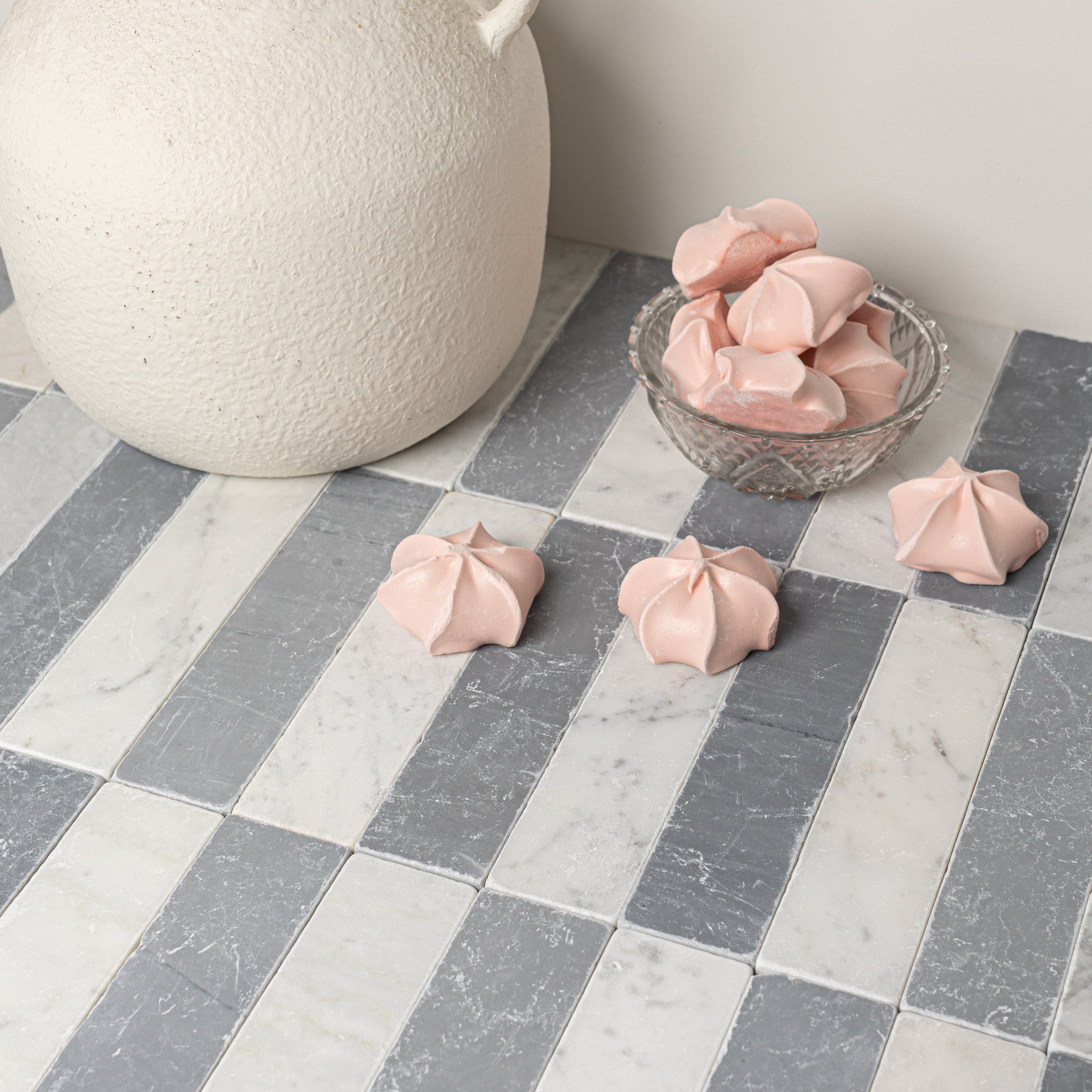 Rectangular tumbled stone tiles in alternating light and dark gray shades with a textured white ceramic vase and pink meringues