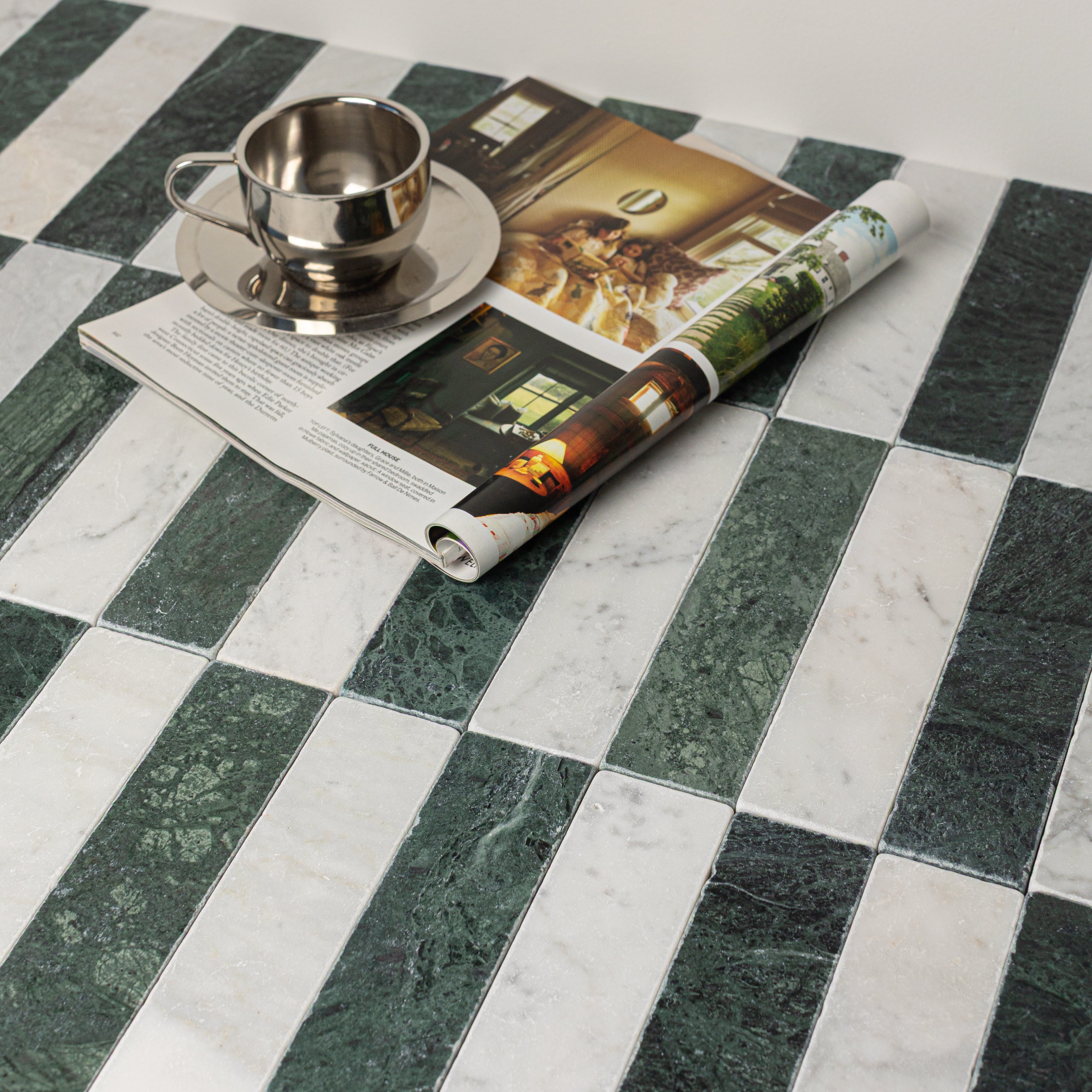 Alternating dark green and white marble rectangular tiles with a metal cup on saucer and an open magazine on top