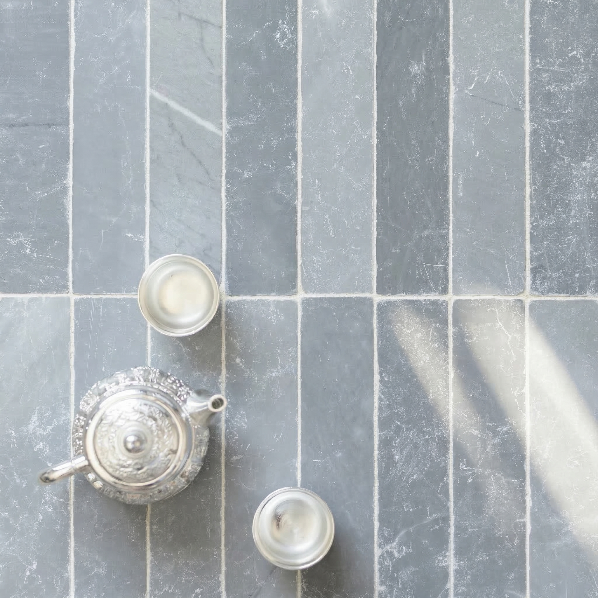 Vertical slate tiles in varied gray tones with natural veining, soft sunlight, and a silver teapot with two cups nearby