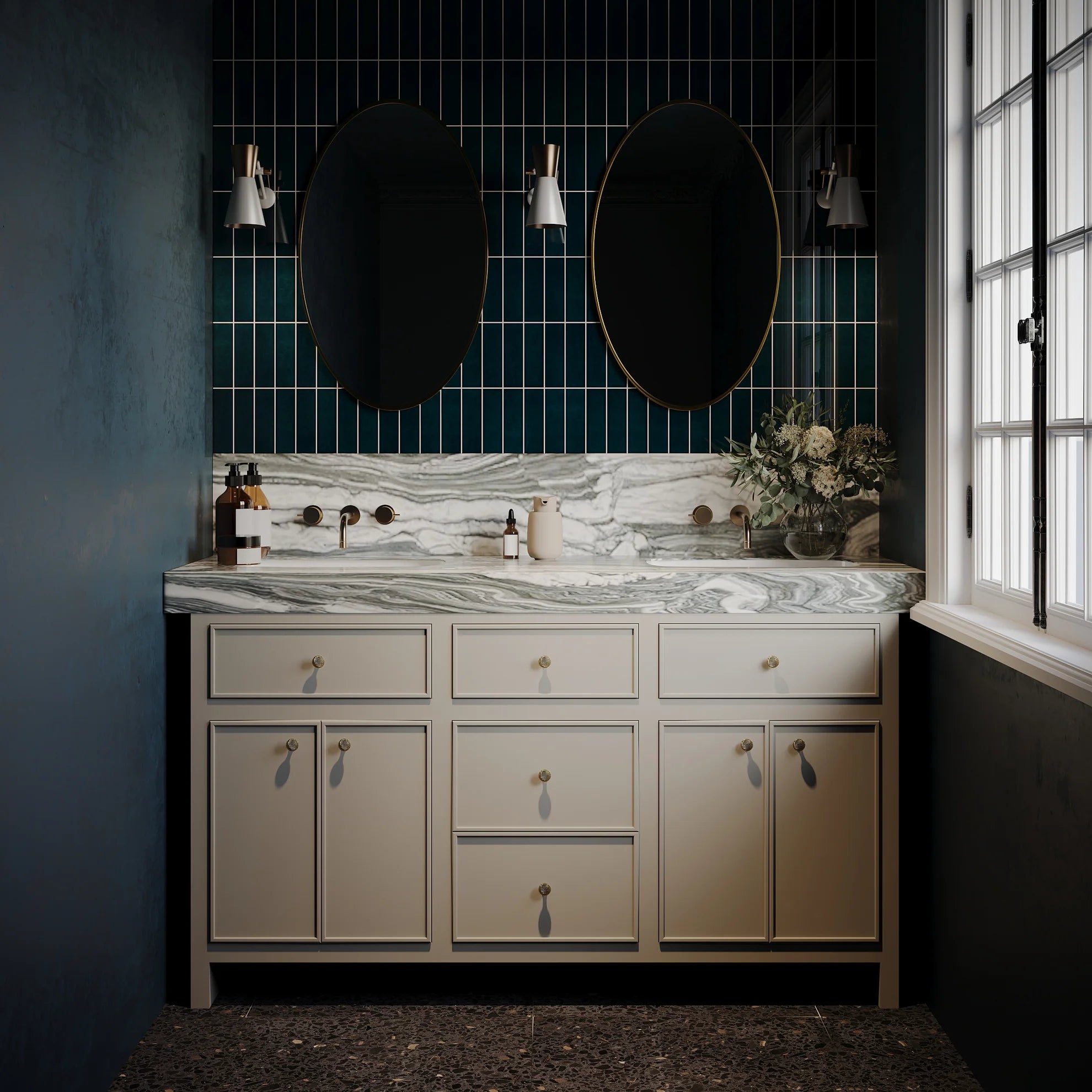 Bathroom vanity with marble countertop, dual sinks, oval mirrors, dark green wall tiles, and decorative plants by window daylight.