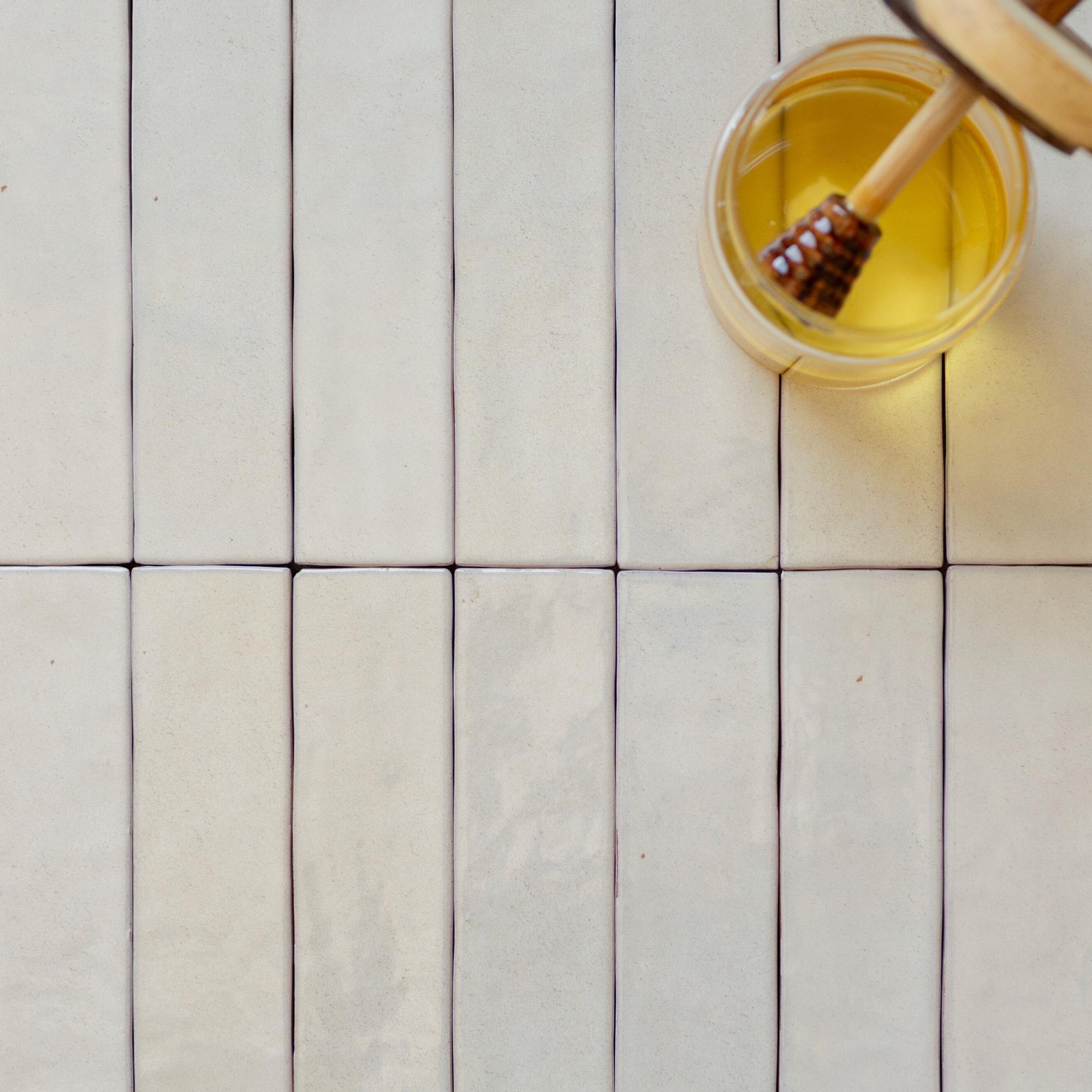 Smooth matte cream rectangular ceramic tiles laid vertically with a honey dipper resting in a glass jar of honey nearby
