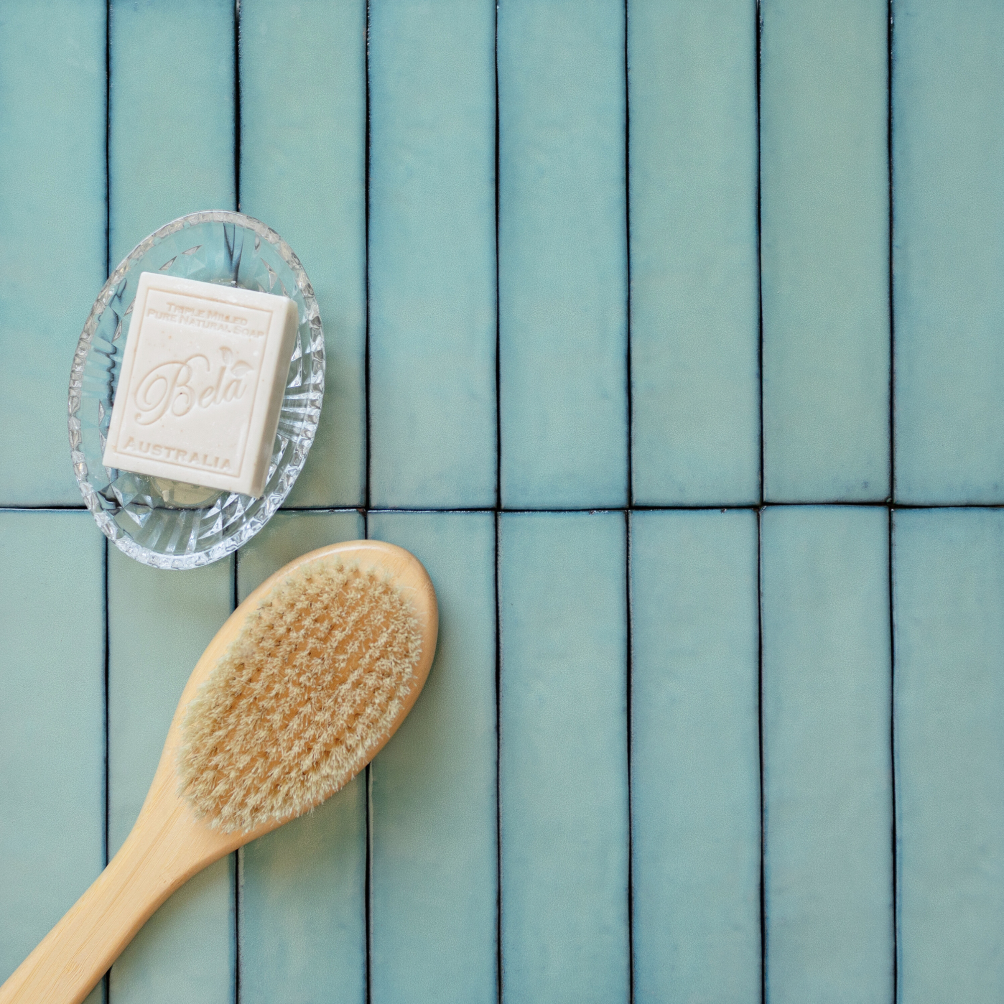 Matte teal elongated rectangular ceramic tiles arranged vertically with a wooden brush and vintage soap in a glass dish nearby