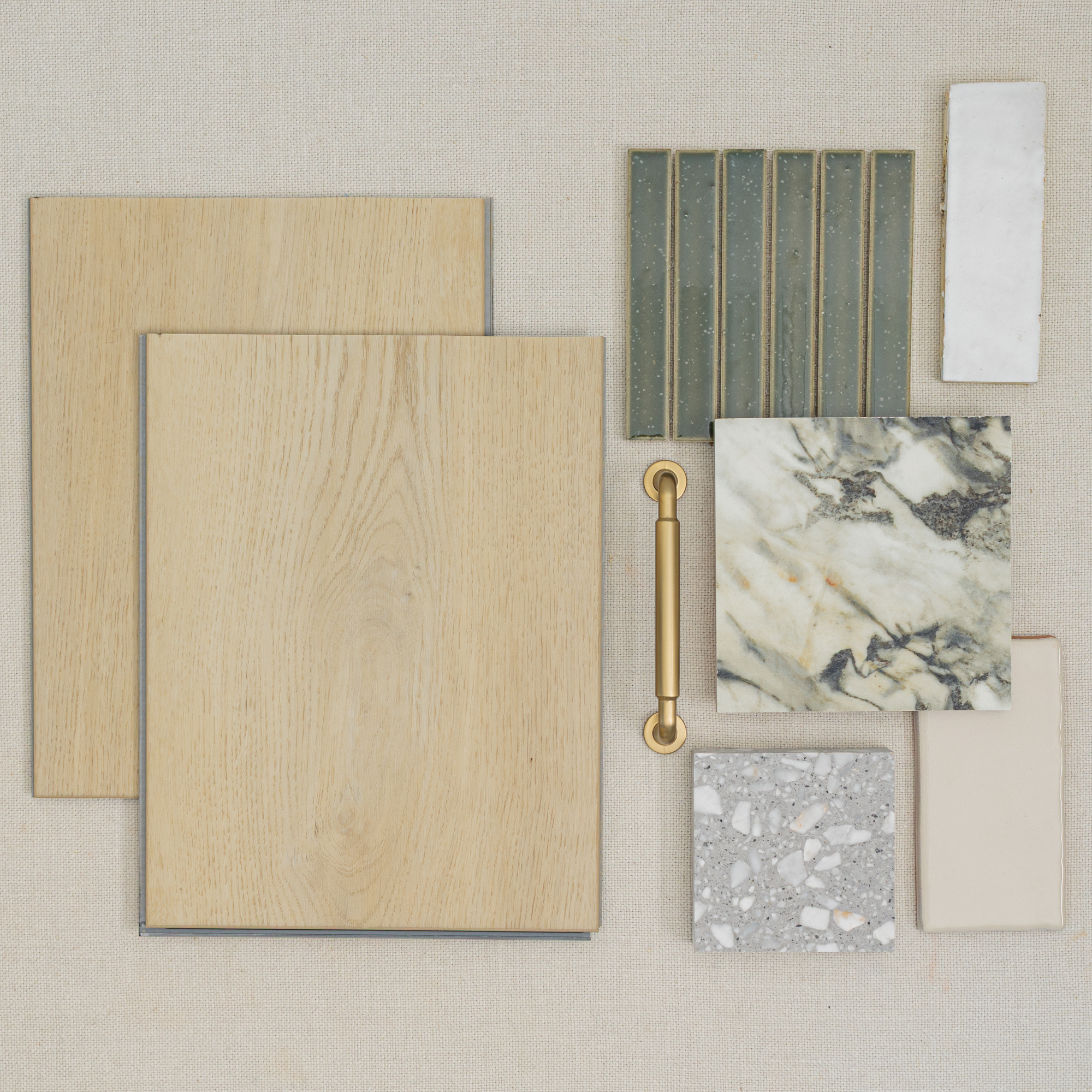 Assortment of wood-look vinyl planks, textured green tiles, marble, terrazzo, and neutral ceramic samples with a gold handle on fabric