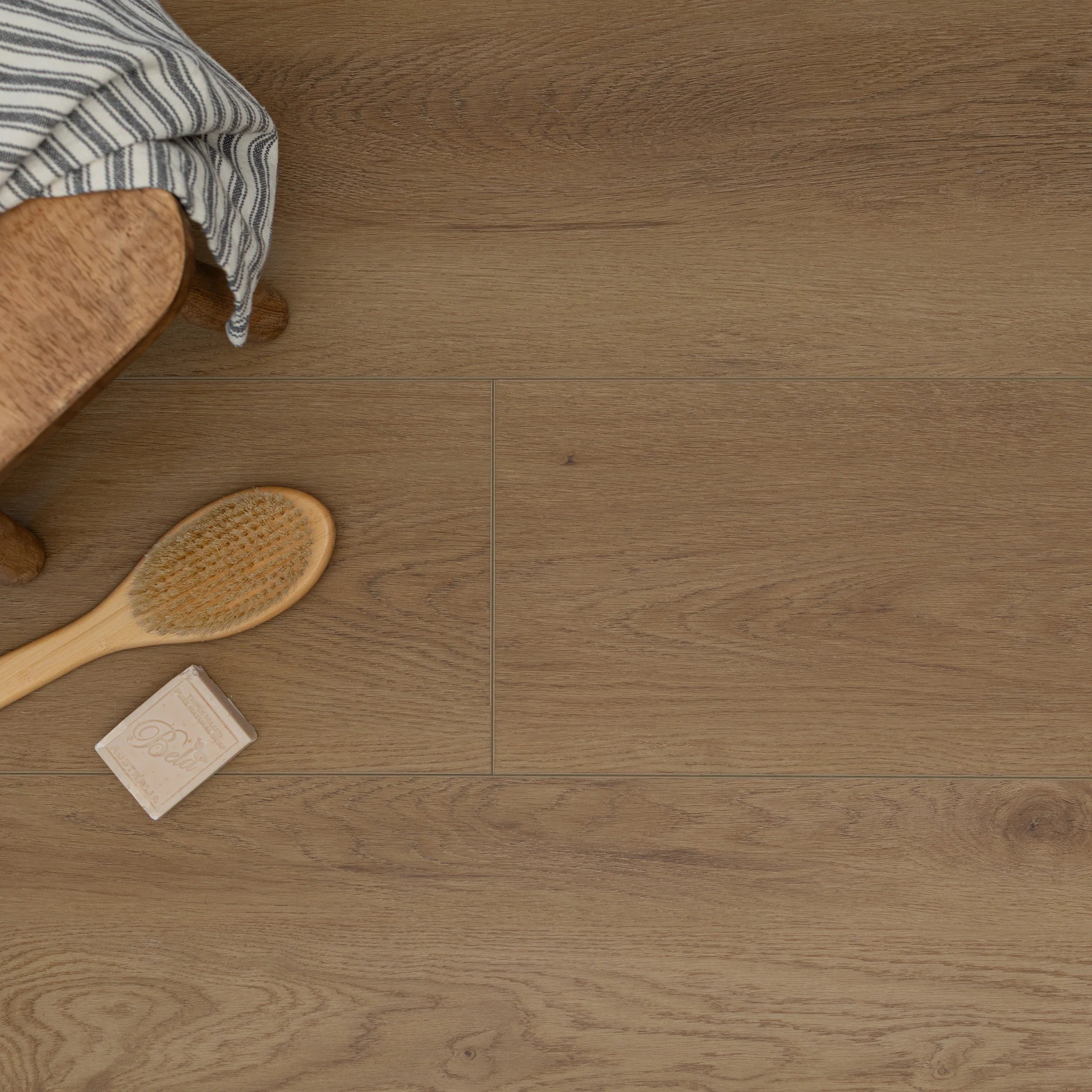 Soft natural oak vinyl flooring with subtle grain and a wooden brush and soap bar on a striped cloth nearby