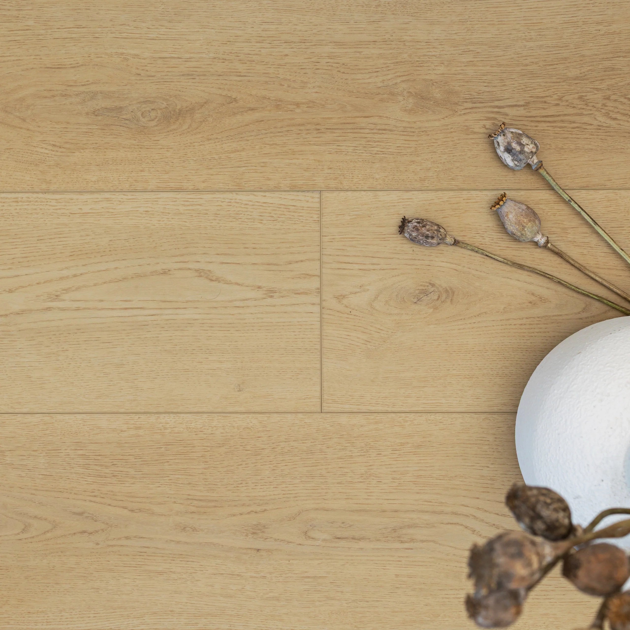 Light wood vinyl flooring with subtle grain texture and dried seed pods arranged beside a white round vase.