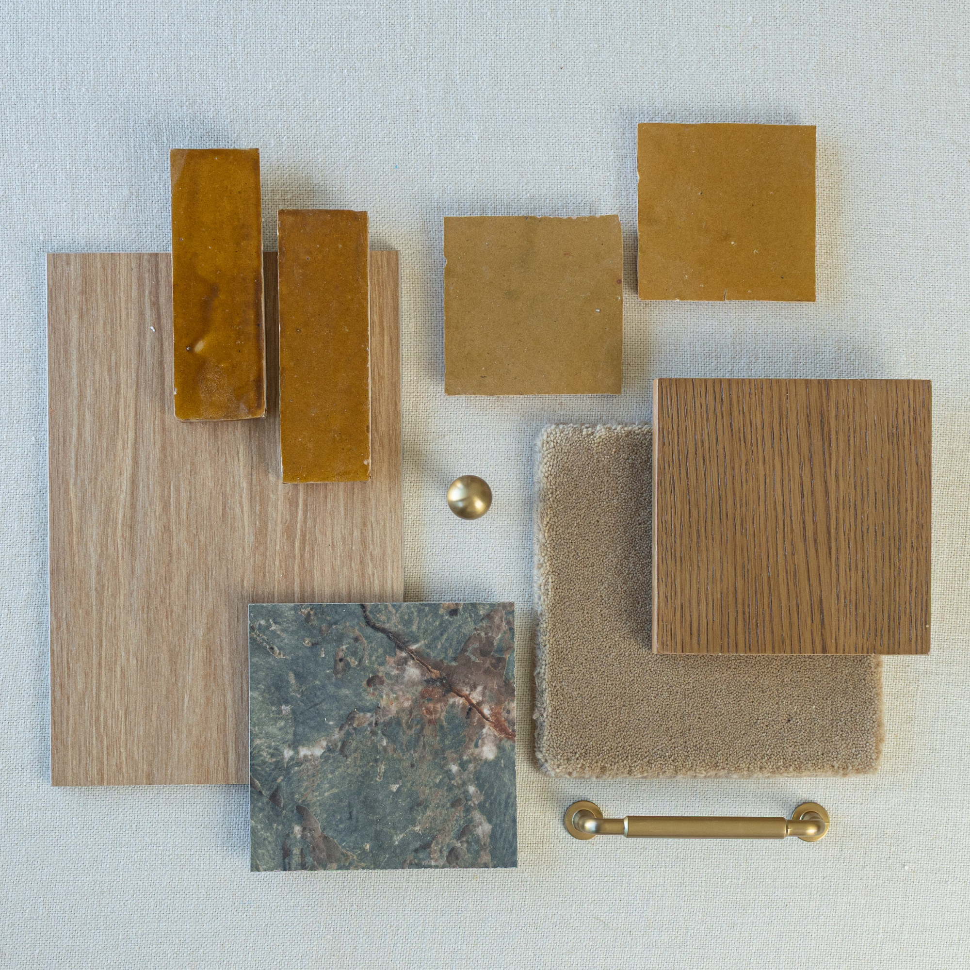 Flat lay featuring caramel glossy ceramic tiles, oak wood samples, textured beige fabric, natural stone tile, and brass hardware on light background