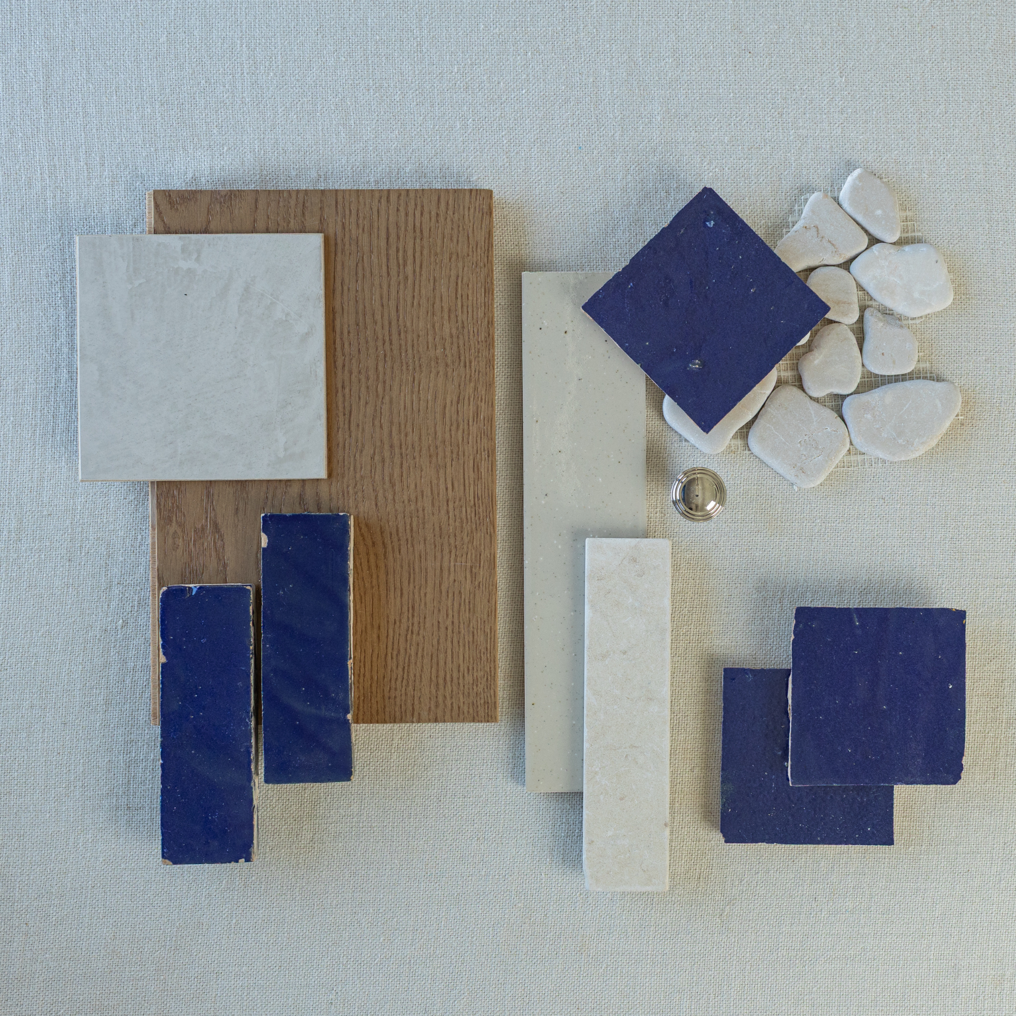 Flat lay of blue and white ceramic tiles, irregular white stones, wood sample, and small metallic knob on fabric background