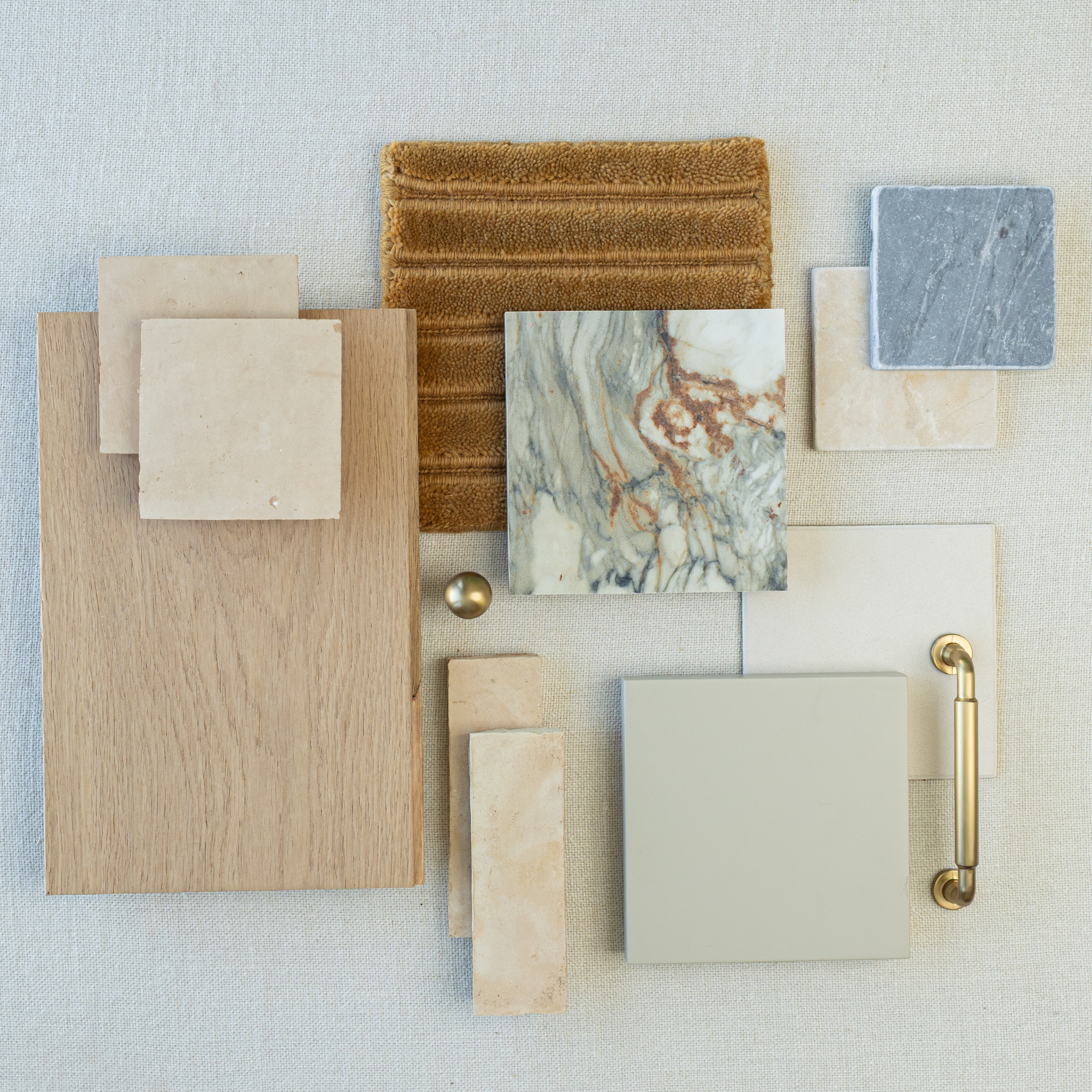 Flat lay of light oak wood, beige and marble stone tiles, textured brown fabric, brass hardware, and gray ceramic tile samples