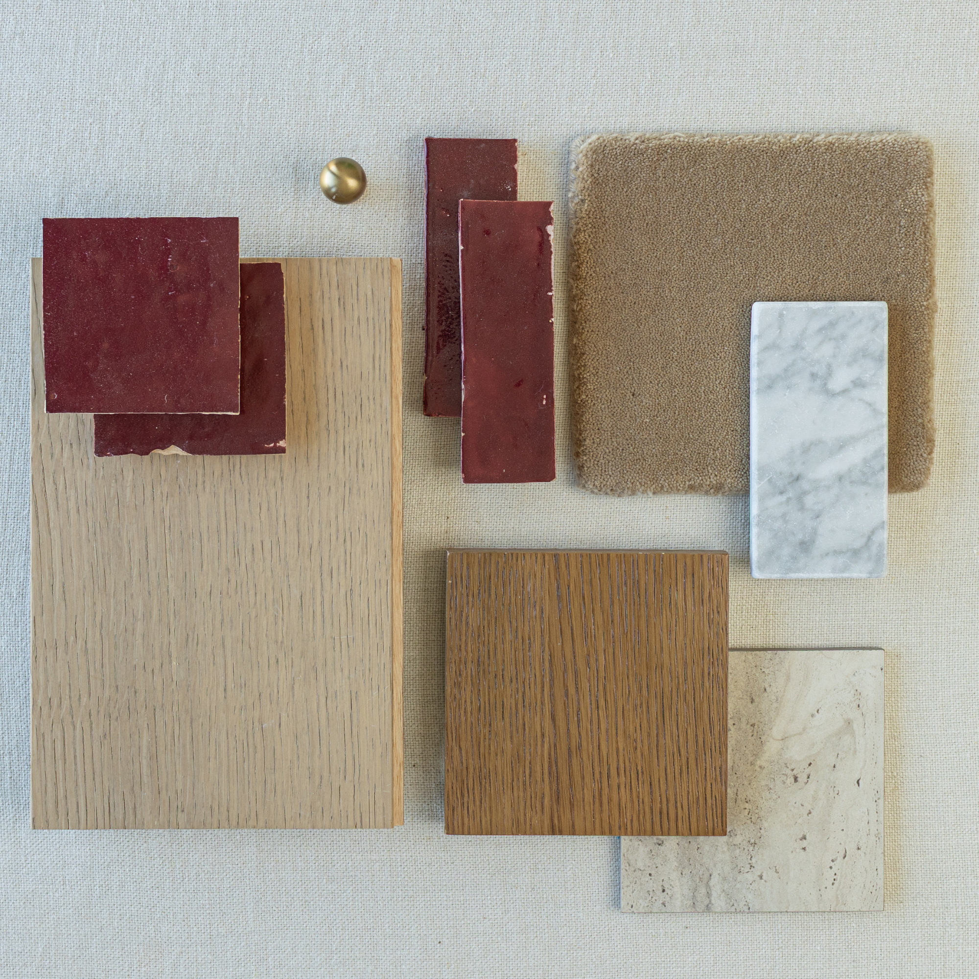 Flat lay of glossy deep red ceramic tiles, oak wood samples, beige fabric swatch, marble and natural stone tiles on light background