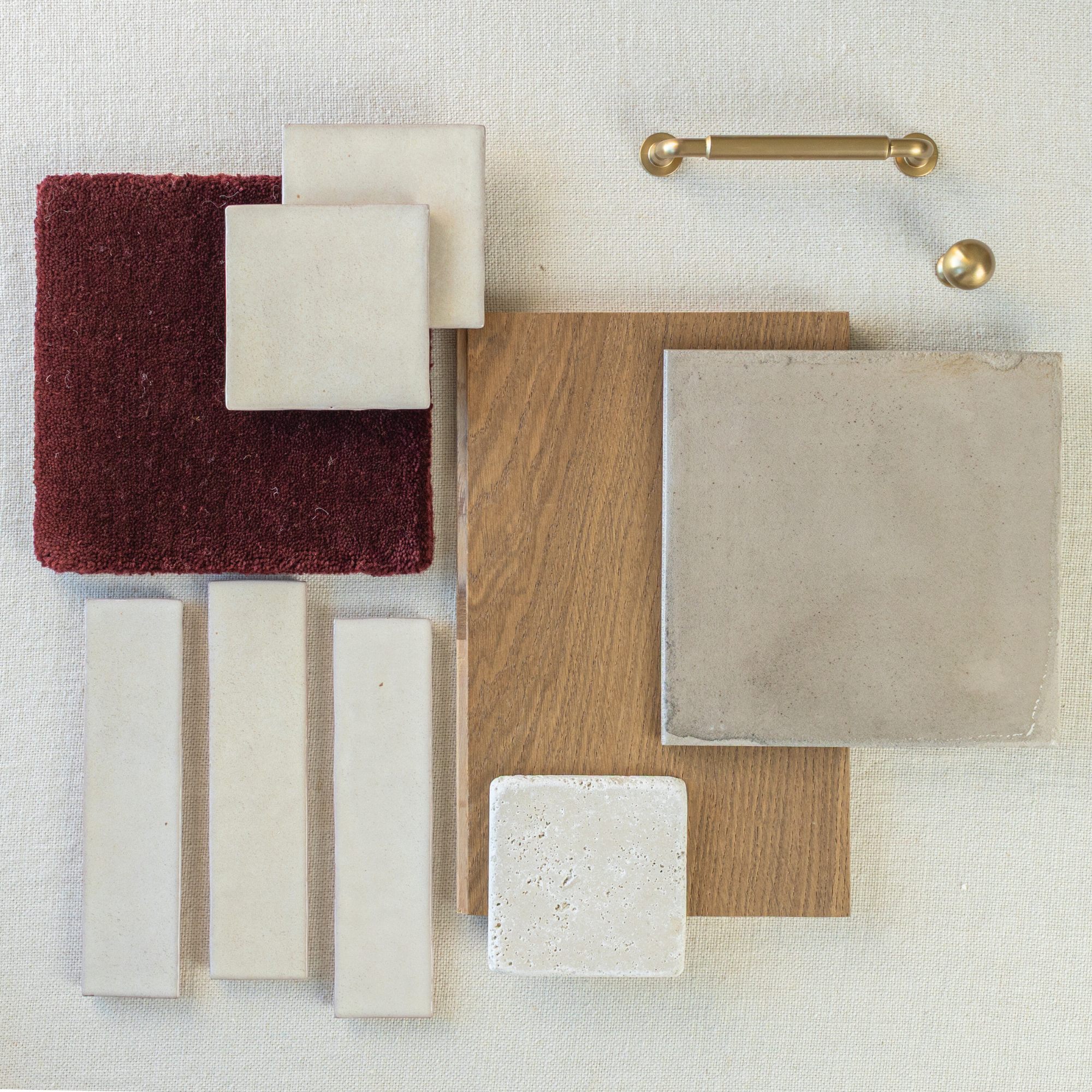 Flat lay of cream ceramic tiles, burgundy carpet swatch, oak wood sample, and brass hardware on beige fabric background