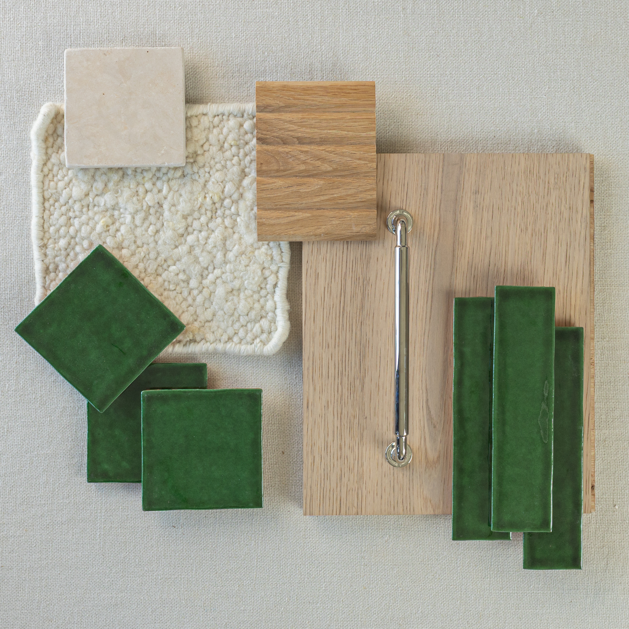 Flat lay of green ceramic tiles, light oak wood samples, chrome handle, and textured cream fabric swatch on neutral background