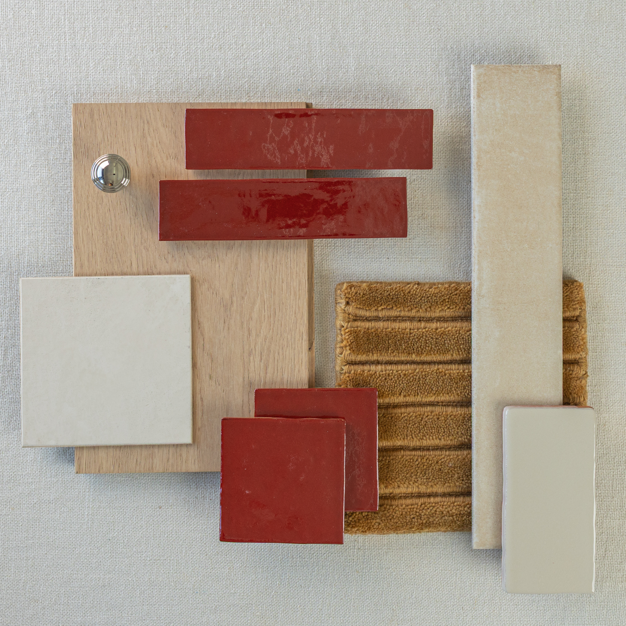 Arrangement of glossy ruby red ceramic tiles, beige porcelain tiles, textured golden fabric, and light oak wood sample on neutral background