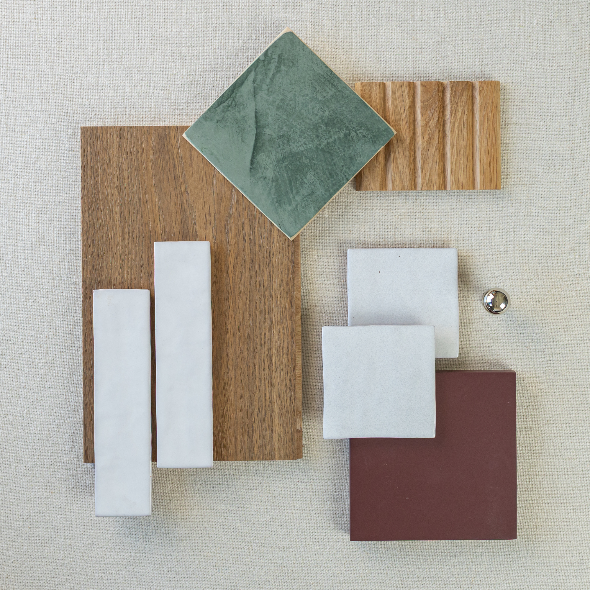 Flat lay of green ceramic tile, white tiles, burgundy square tile, wood samples, and metal knob on beige fabric background