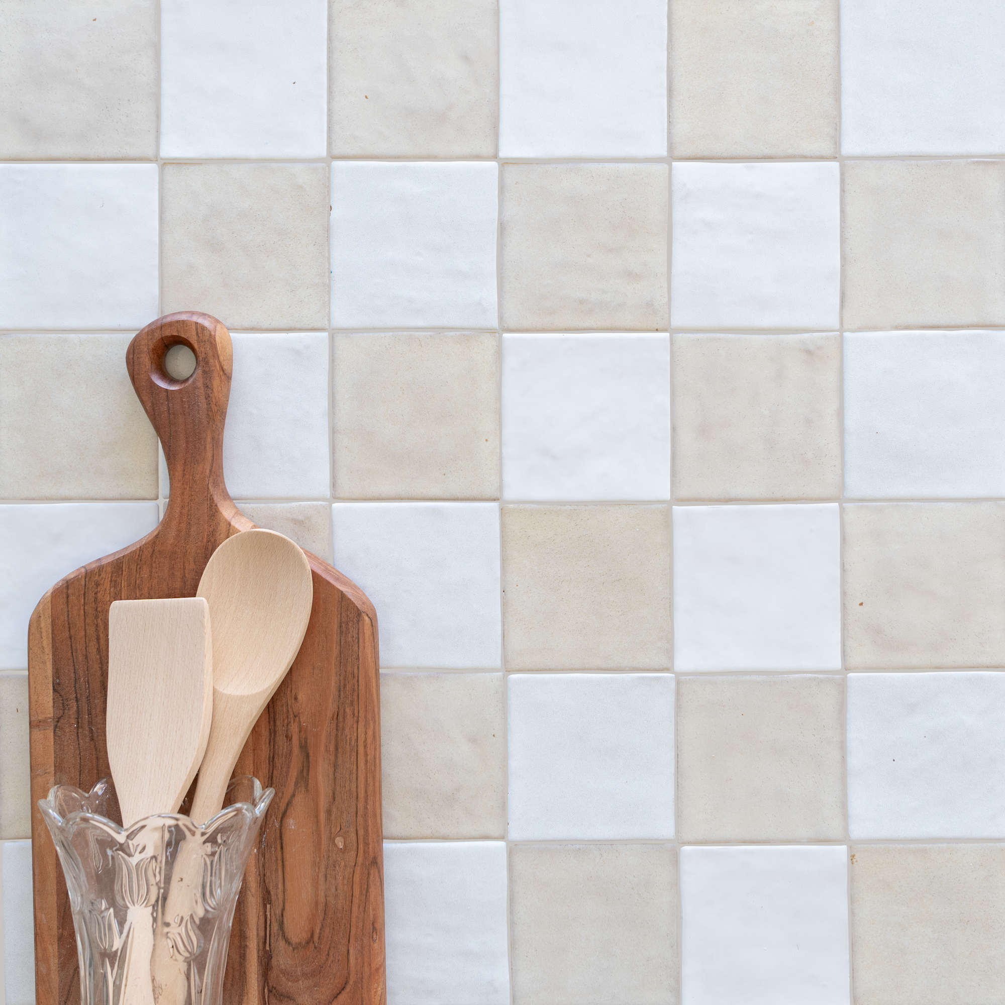 Square ceramic tiles in soft beige and white alternating pattern with wooden kitchen utensils on a cutting board