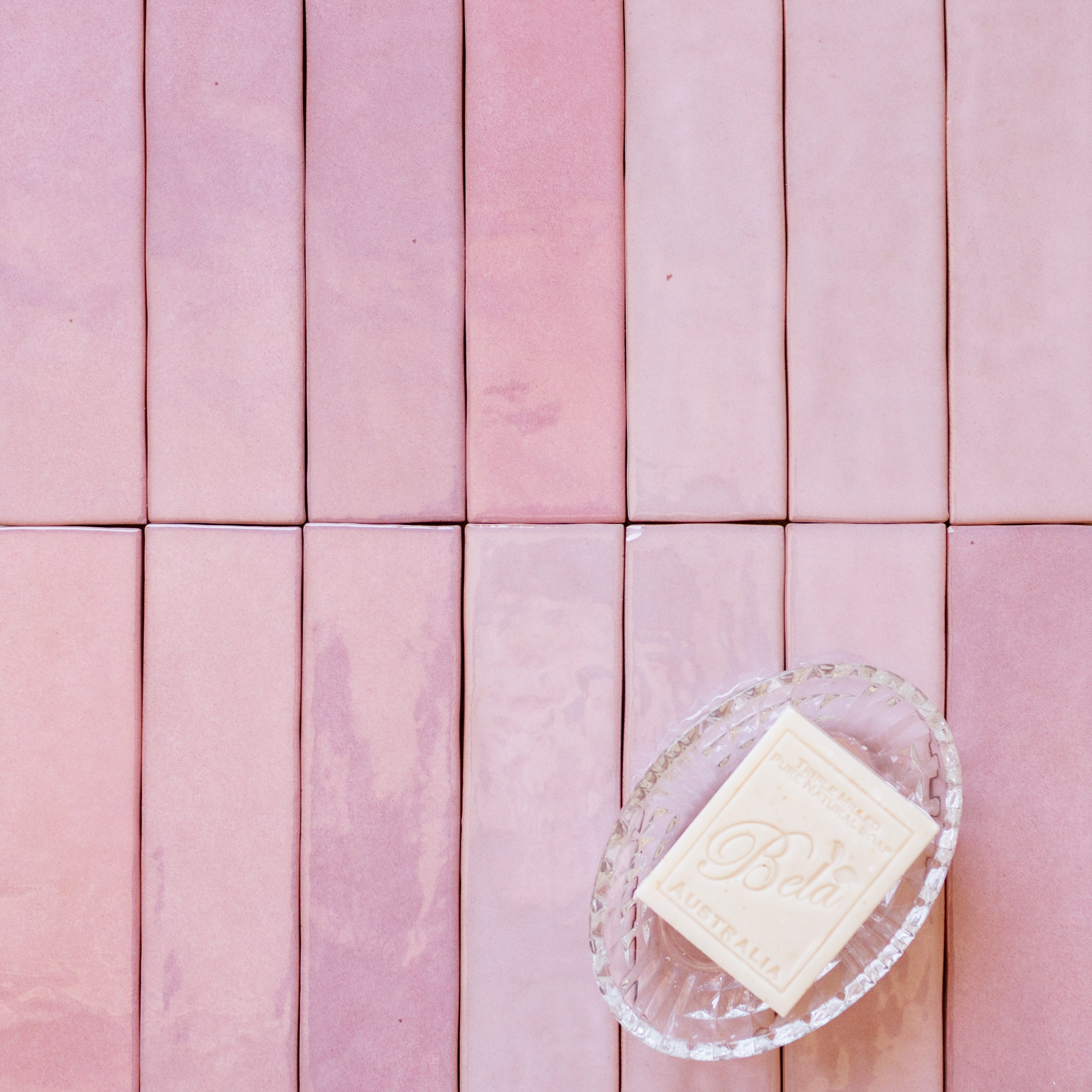 Rectangular pink ceramic tiles with varying shades arranged in a grid with a clear dish holding a white soap bar.