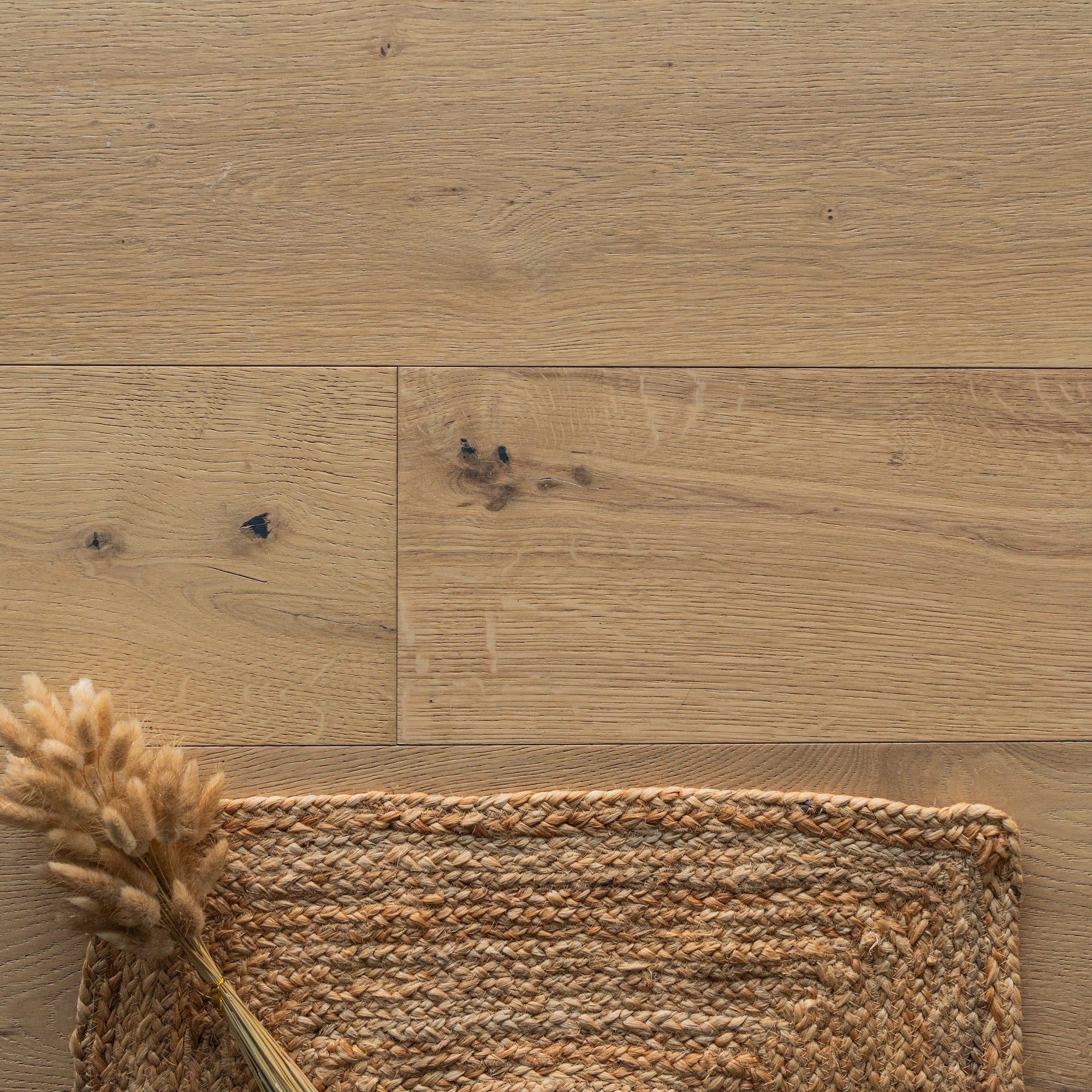 Top view of natural oak wood flooring with textured woven mat and dried floral arrangement in bottom corner