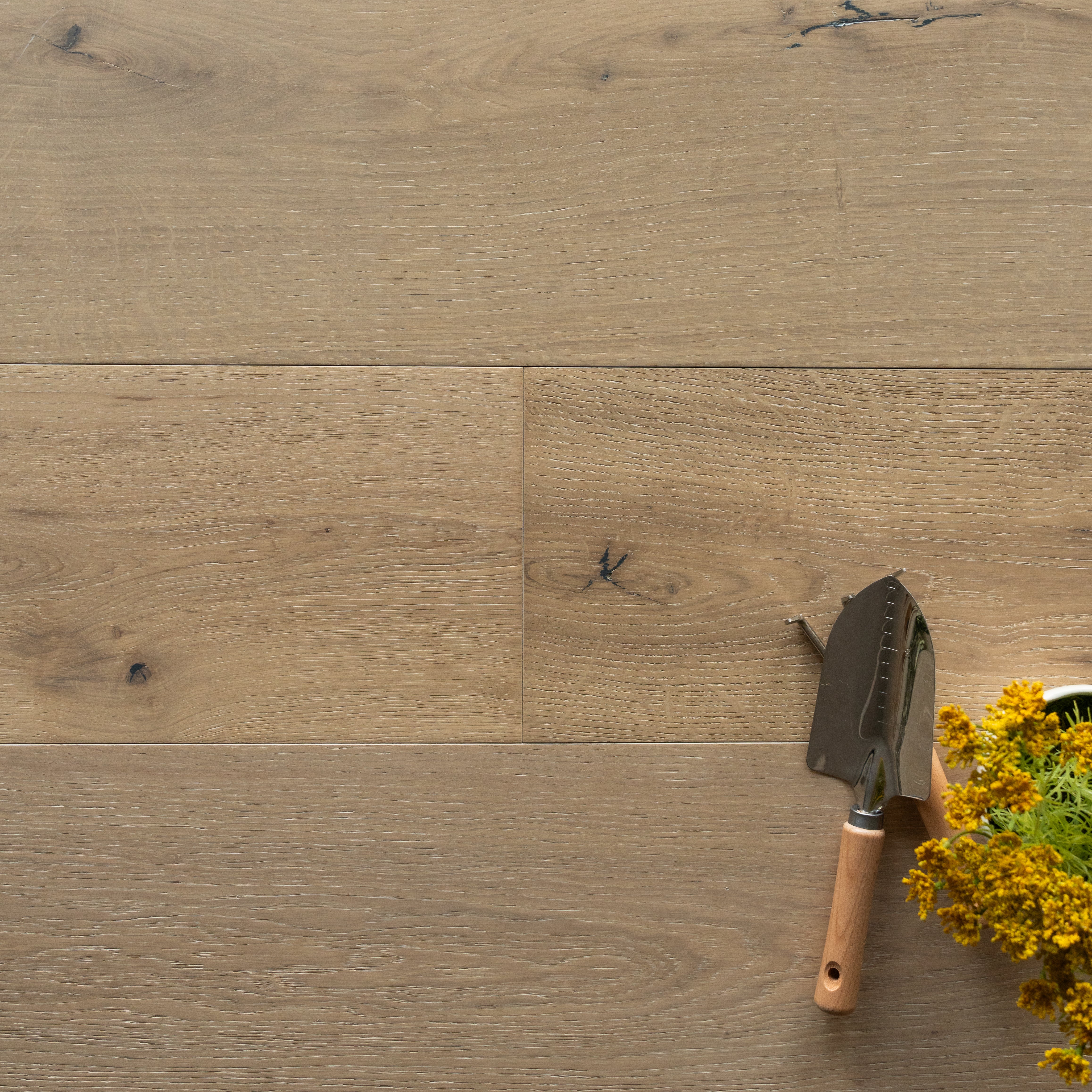 Close-up of light oak flooring with small gardening trowel and cluster of yellow flowers on the side