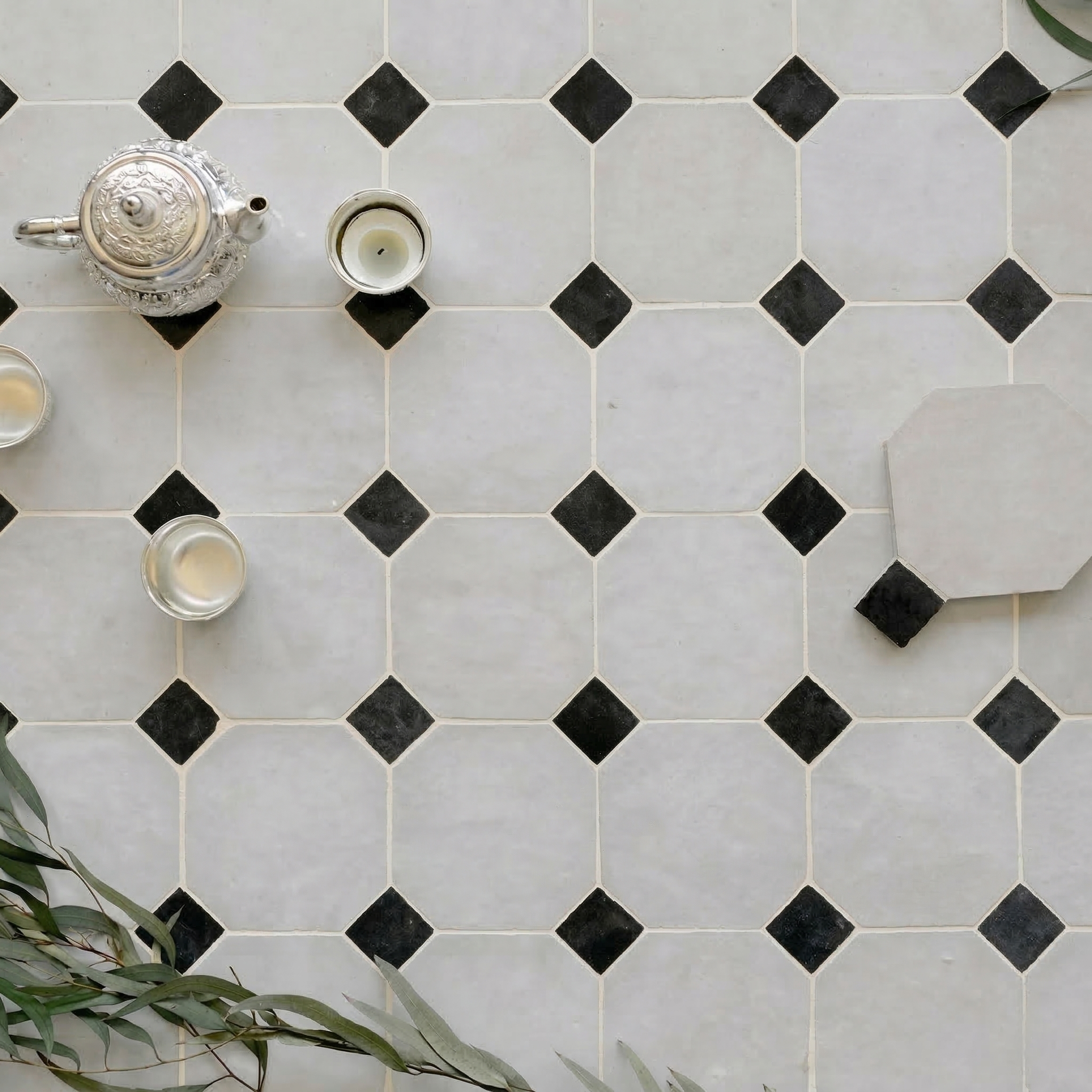 Soft matte ceramic flooring with large light tiles accented by small black diamond shapes and silver tea set nearby